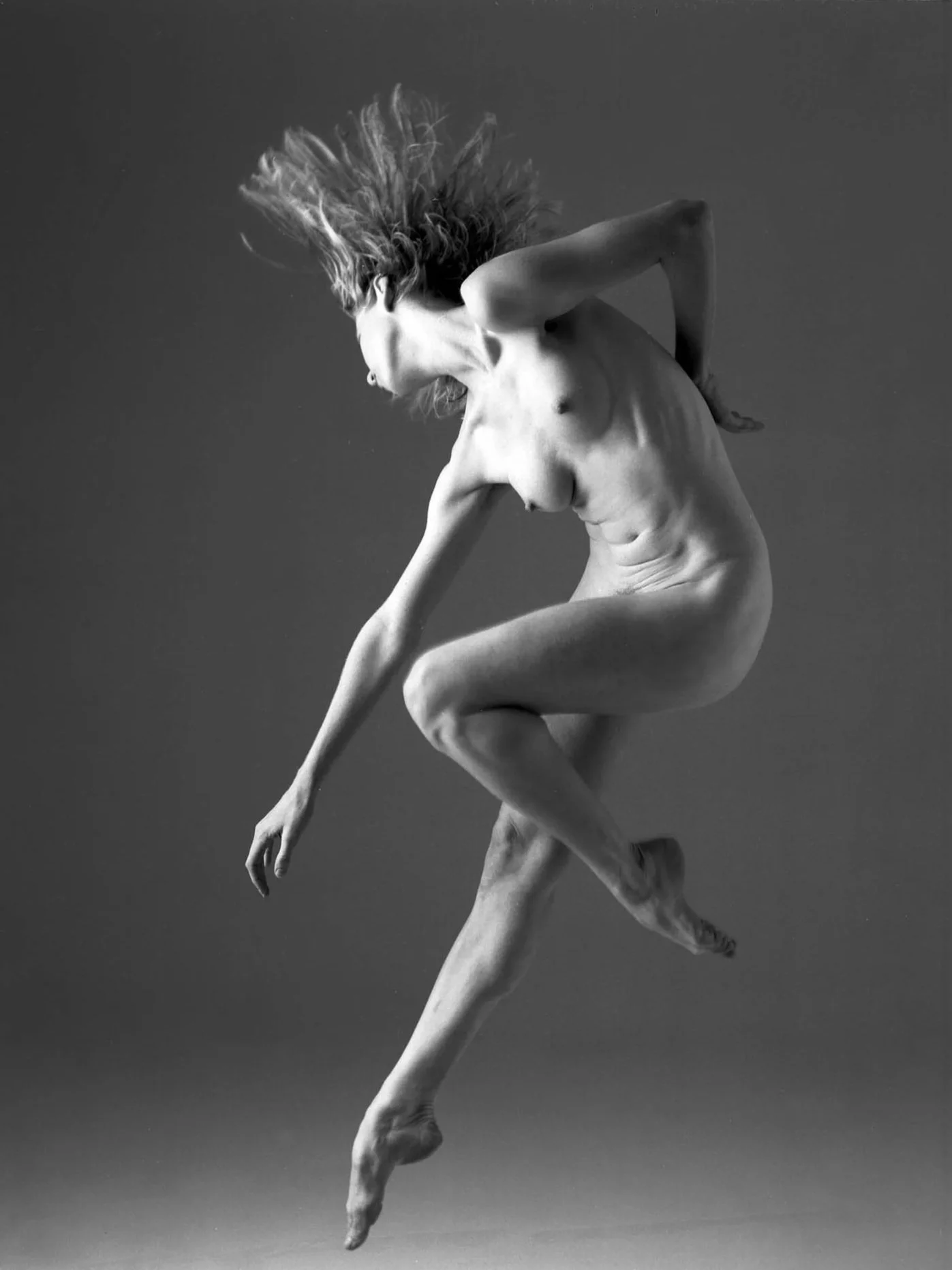 A nude dancer is jumping in the air