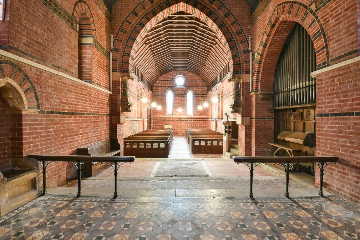 A typical small mid-Victorian chapel of yellow brick with bands of red and black brick and minimal stone dressings, red brick double modillion cornice and stone window heads and cills and a tiled roof. The chancel arch is of two main orders support