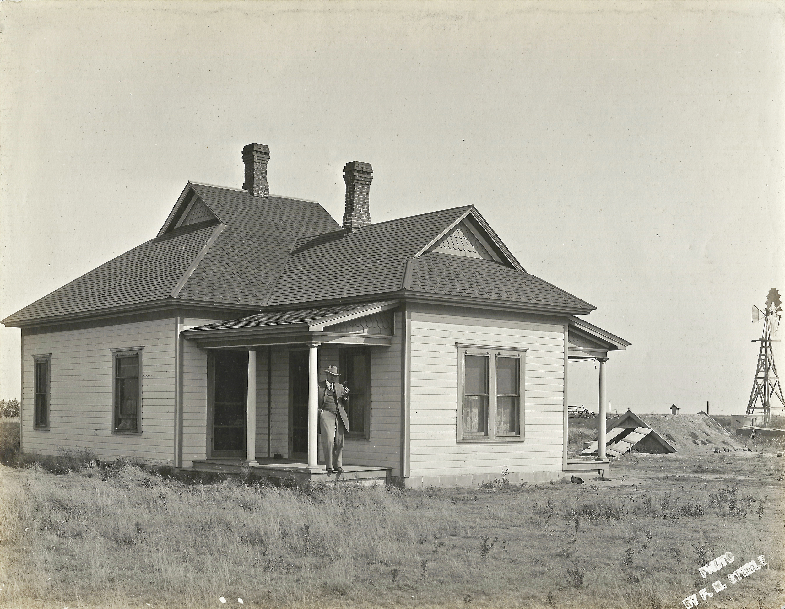 F. E. "Gene" Murphy is shown on the porch of his ranch house which he built in 1908. He once owned 100 quarter-sections of Haskell County land. This house located east of Santa Fe, later became the home of Harold Walters. Note, the storm cellar, or "fraid hole" right.