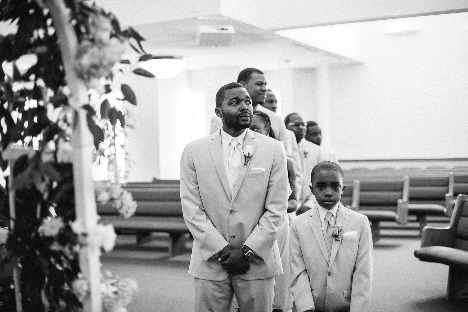 Teary eyed groom watches bride walk down the aisle of a church next to ring bearer