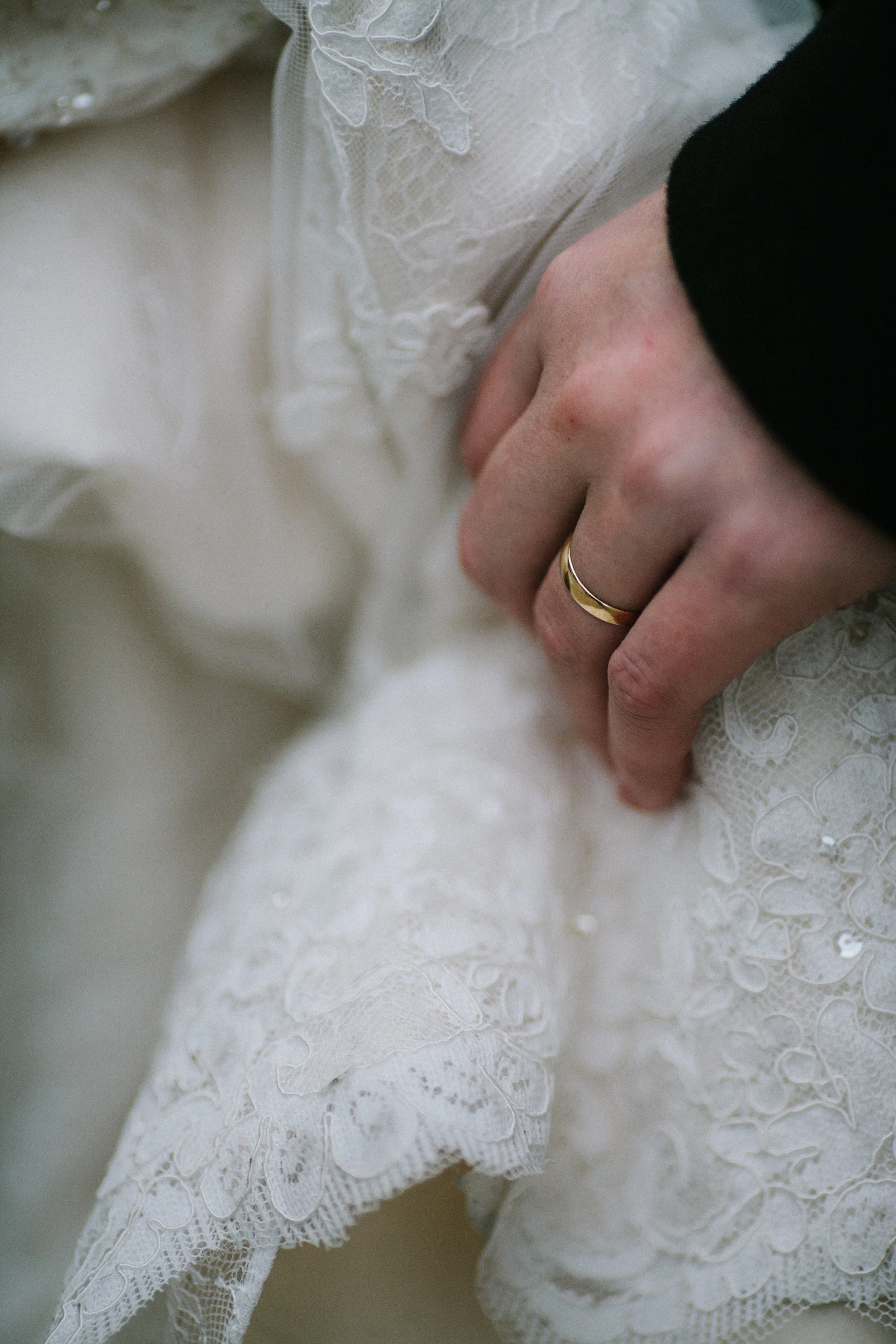 Groom's hand with wedding ring holds onto the bride's lace dress