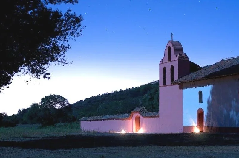 Church at La Purisima Mission at night with the glow of lanterns.