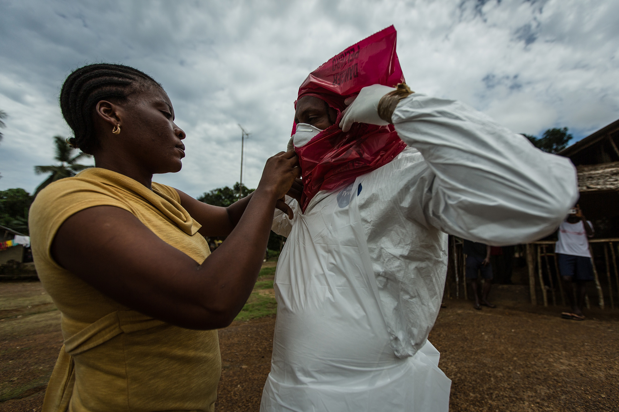  Varbah helps seal Melvin's Personal Protective Equipment (PPE) as he suits up to remove the body of Phelica Anthon,&nbsp;6,&nbsp;in Arthingon, Liberia.&nbsp; 