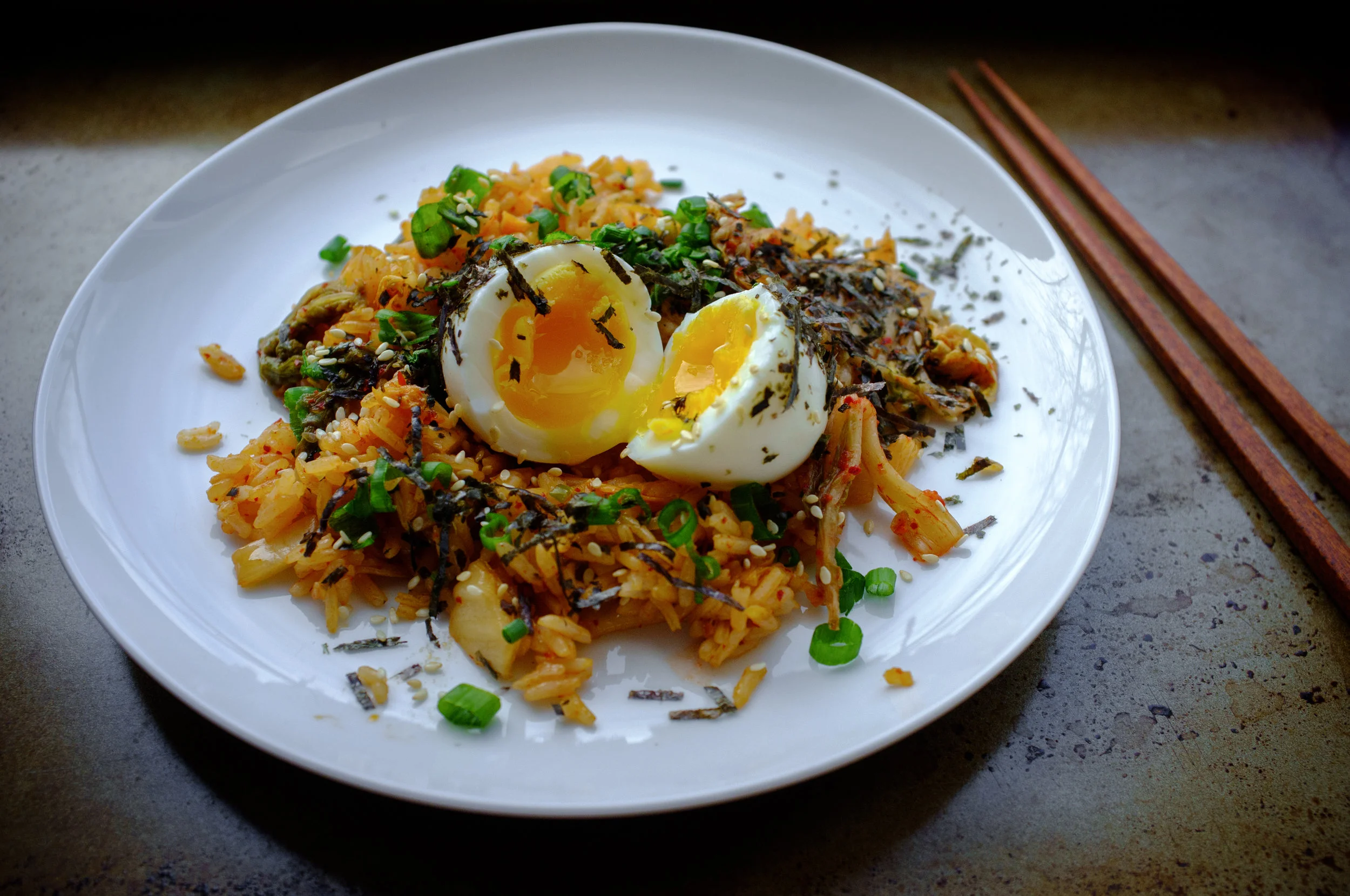 Kimchi fried rice with a soft boiled egg, garnished with shredded seaweed, sesame seeds and scallion greens