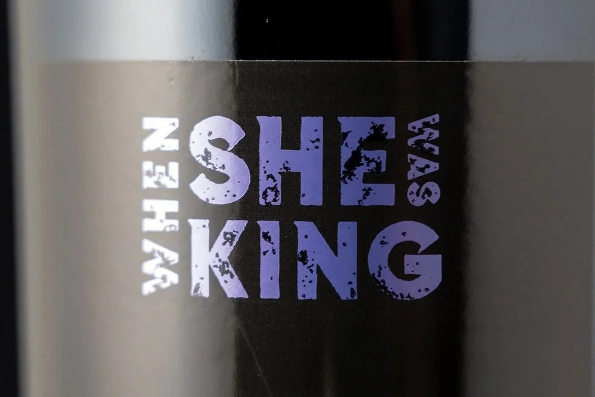 Close-up of a black container with purple and white text that reads "WE HELP SHE SAY KIN" in a distressed font.
