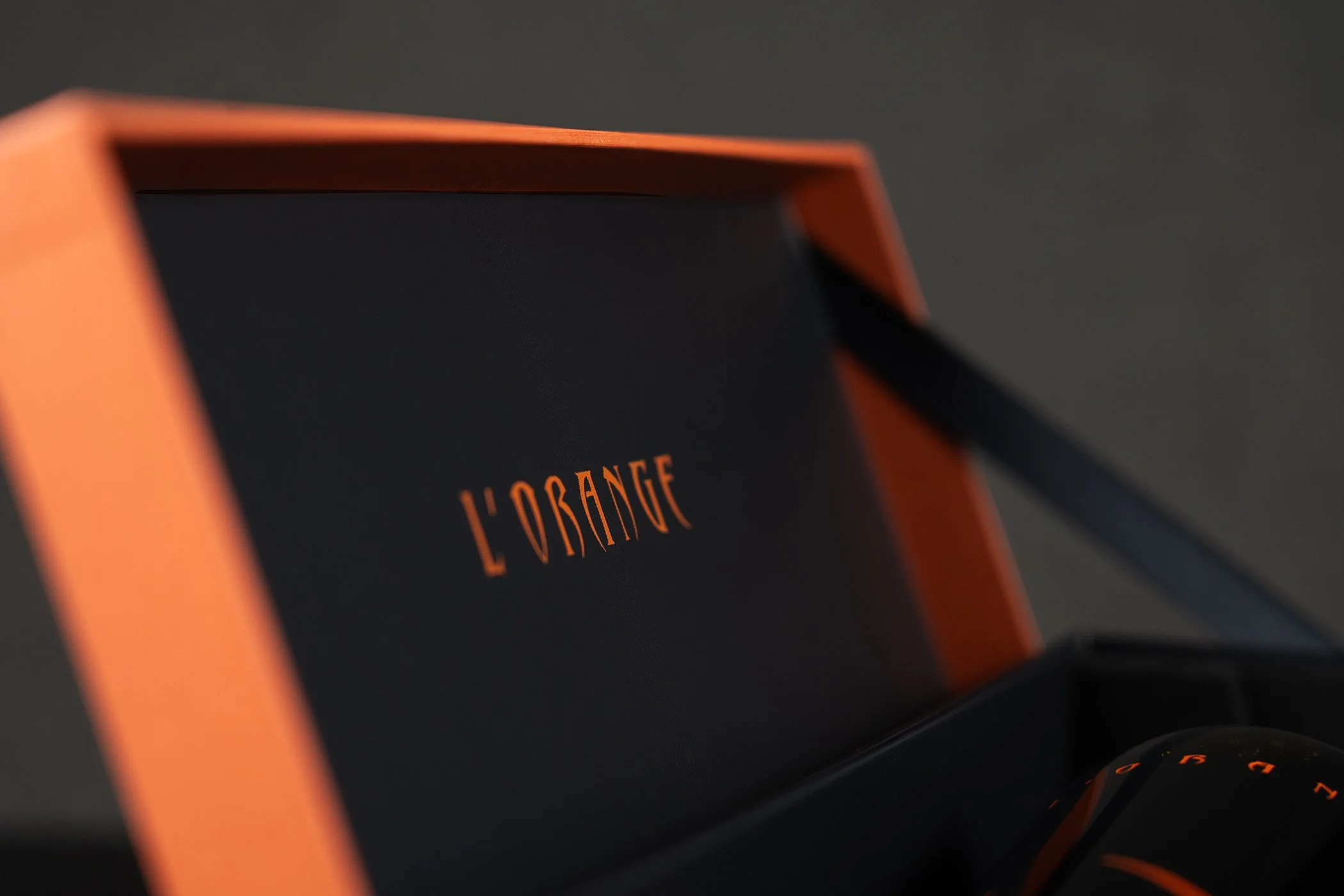 Close-up of a fashion item with orange framing and black fabric, the text 'L'ORANGE' visible on the black fabric.