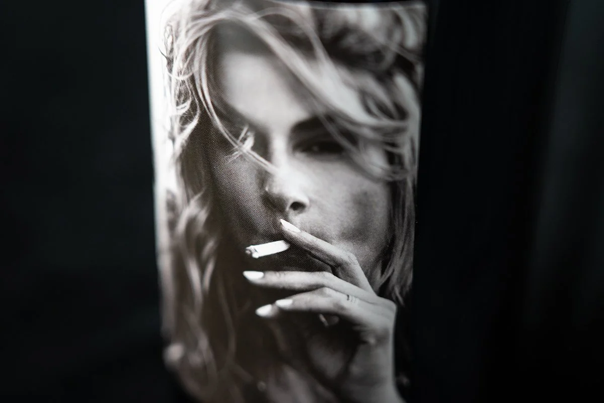Black and white photo of a woman with tousled hair holding a cigarette near her lips.