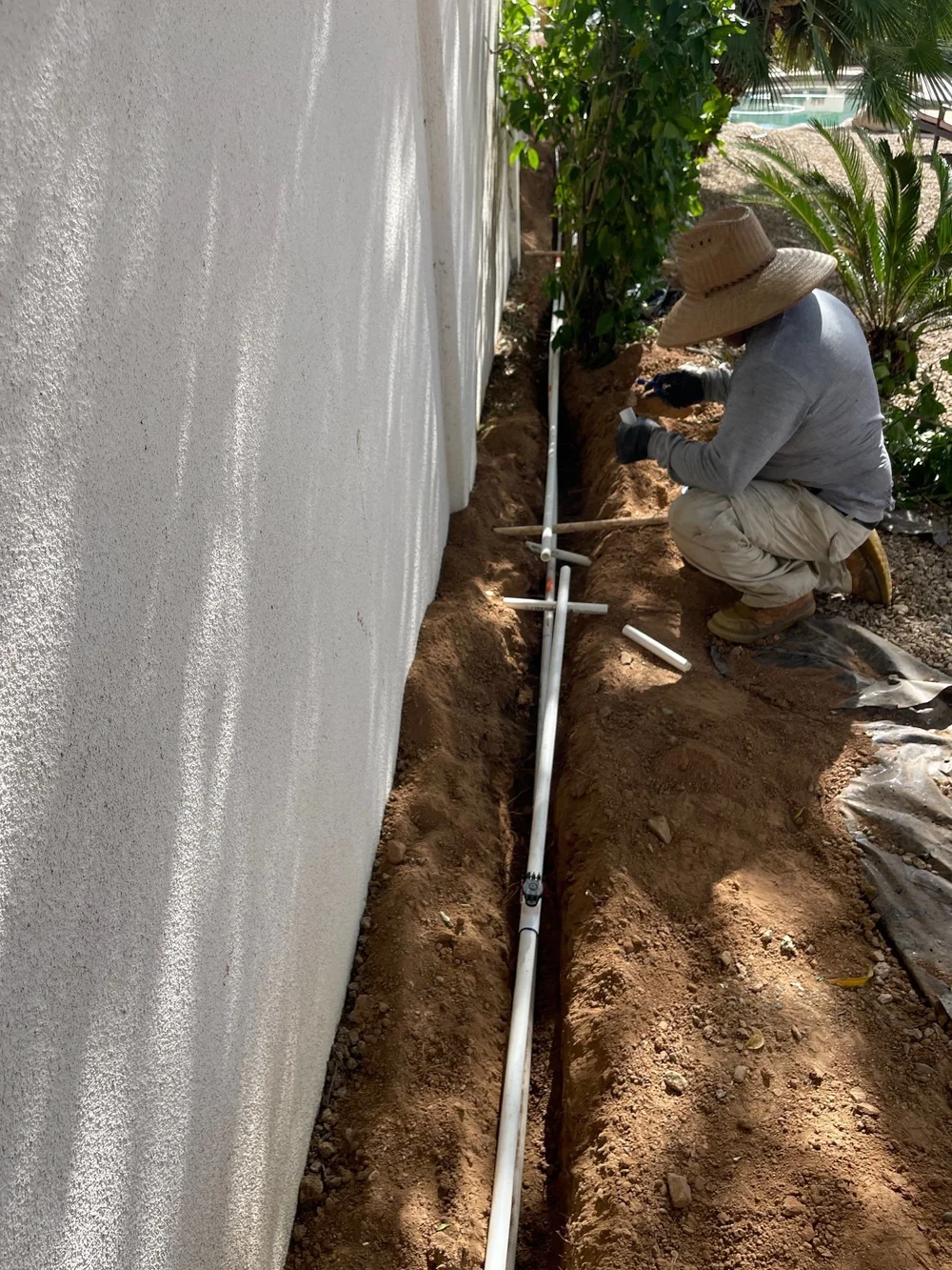 Blooming Valley Landscape crew member installing PVC irrigation pipe in a trench