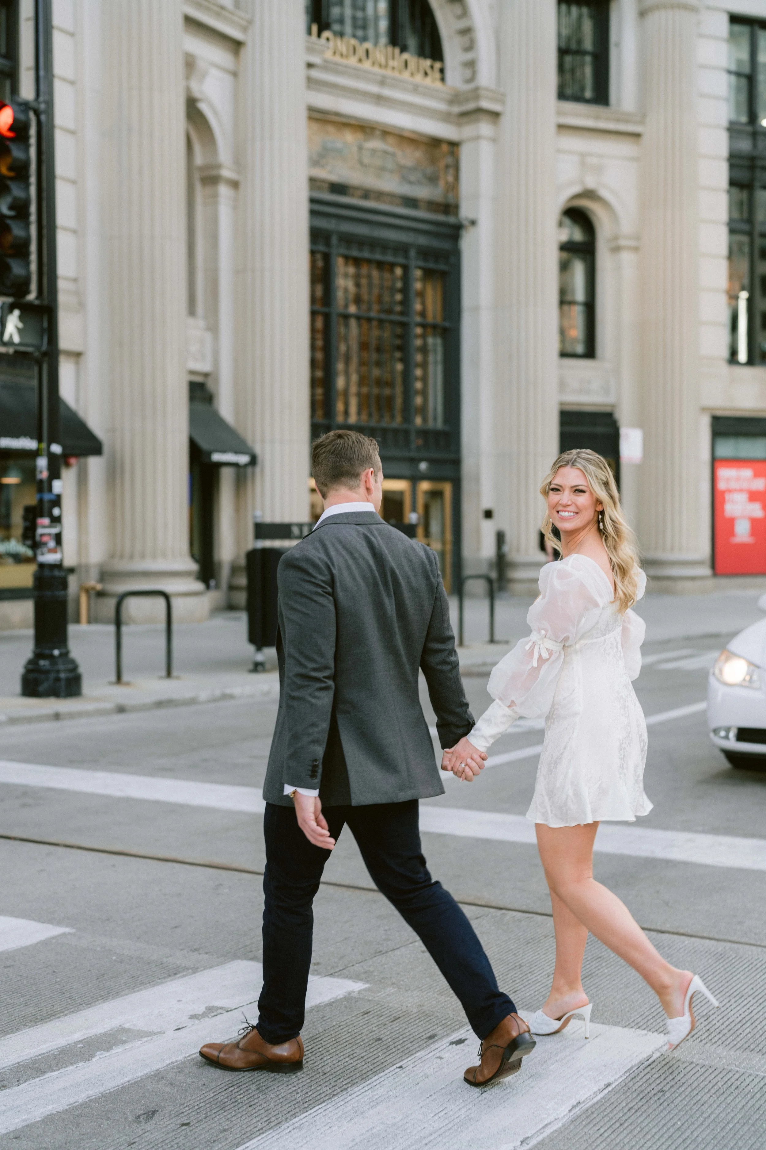 couple holds hands crossing the street as they walk down to the chicago river for engagement photos