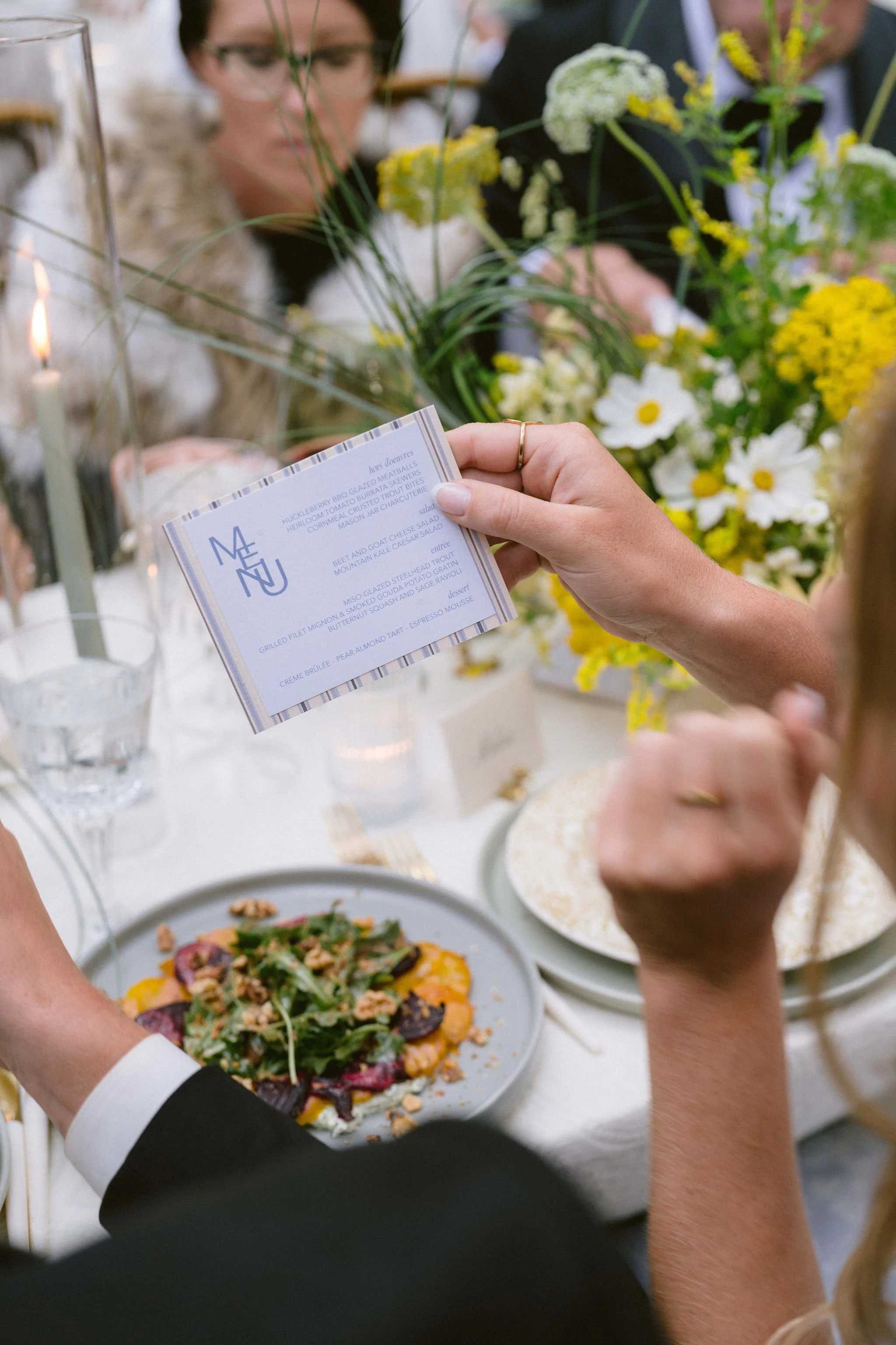 guests look over the menu for the wedding reception dinner with a beet salad in the background on the table