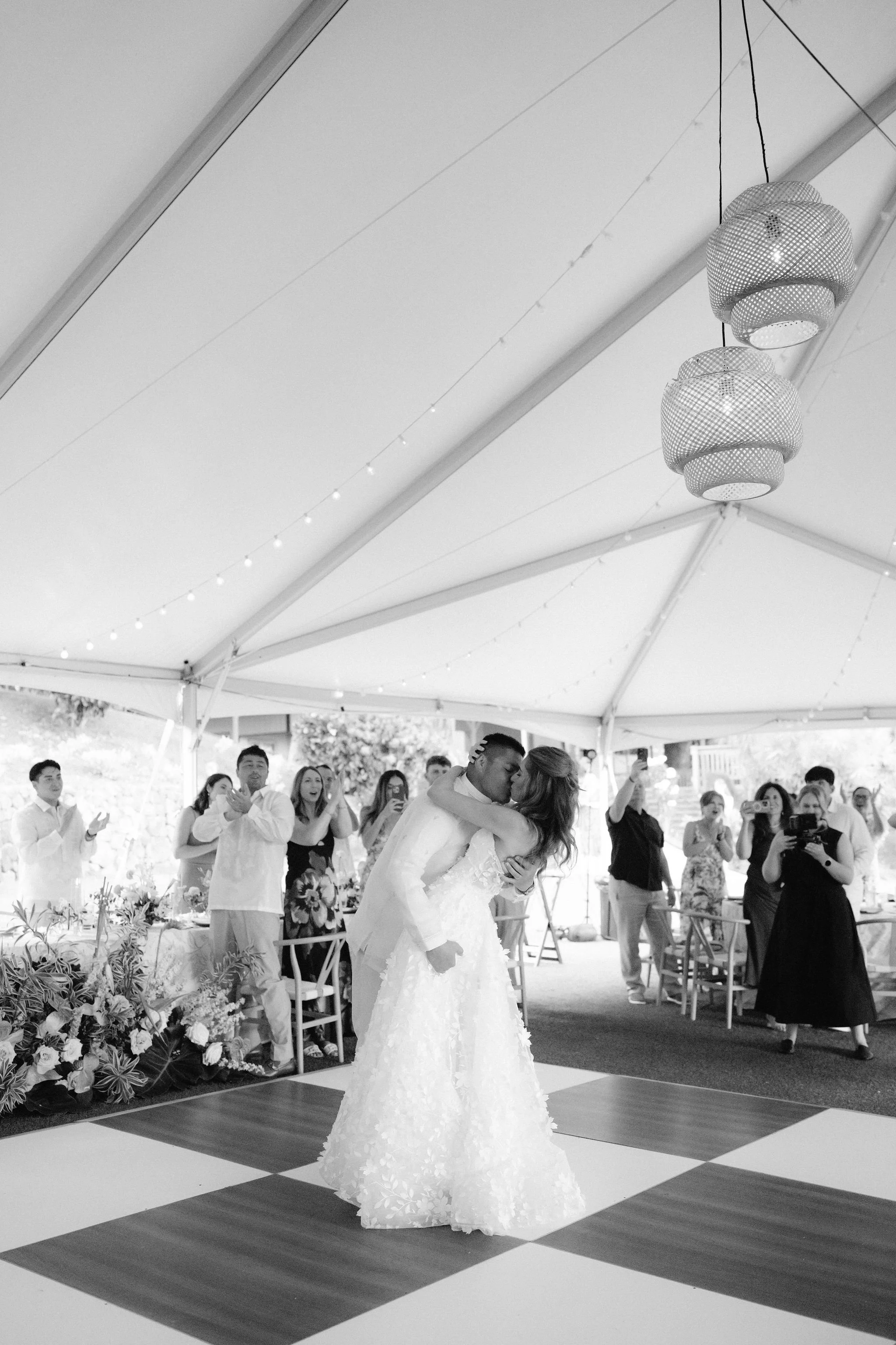 bride and groom kiss on black and white check dance floor under the tent at kualoa ranch wedding