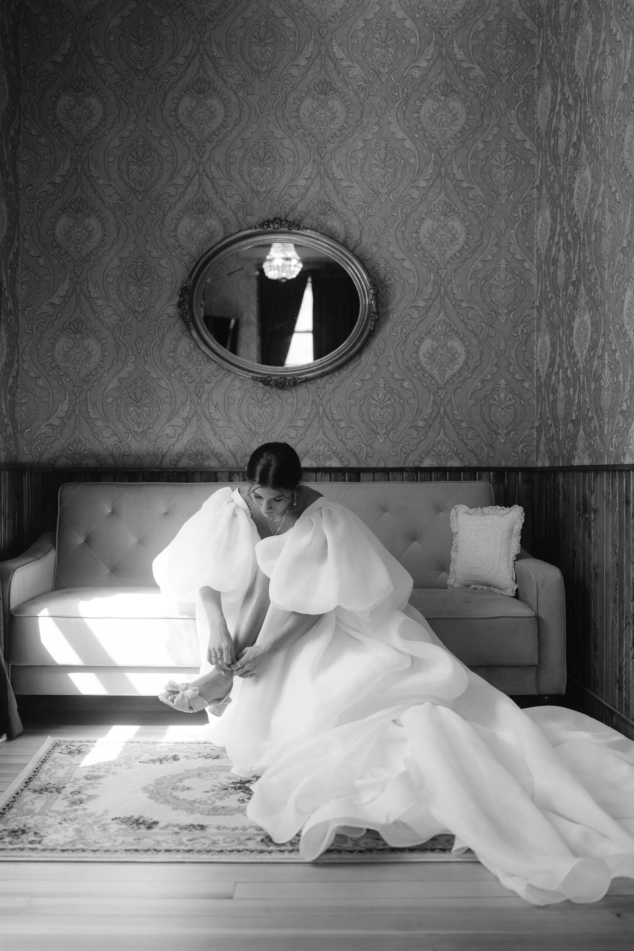 bride sits on a setee as she hooks her shoes after getting into her wedding gown