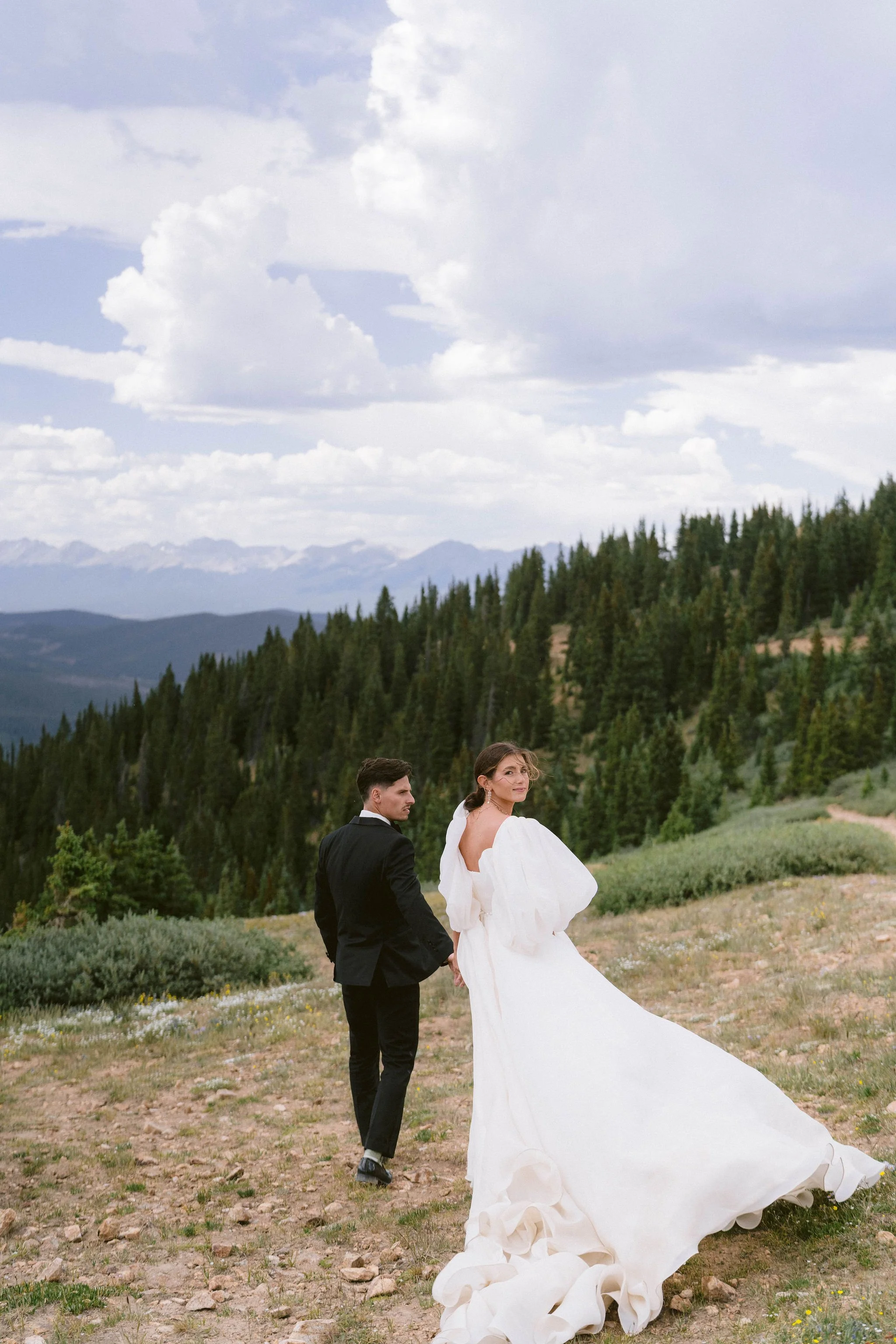 bride and groom walk hand in hand at the top of a mountain pass on their wedding day