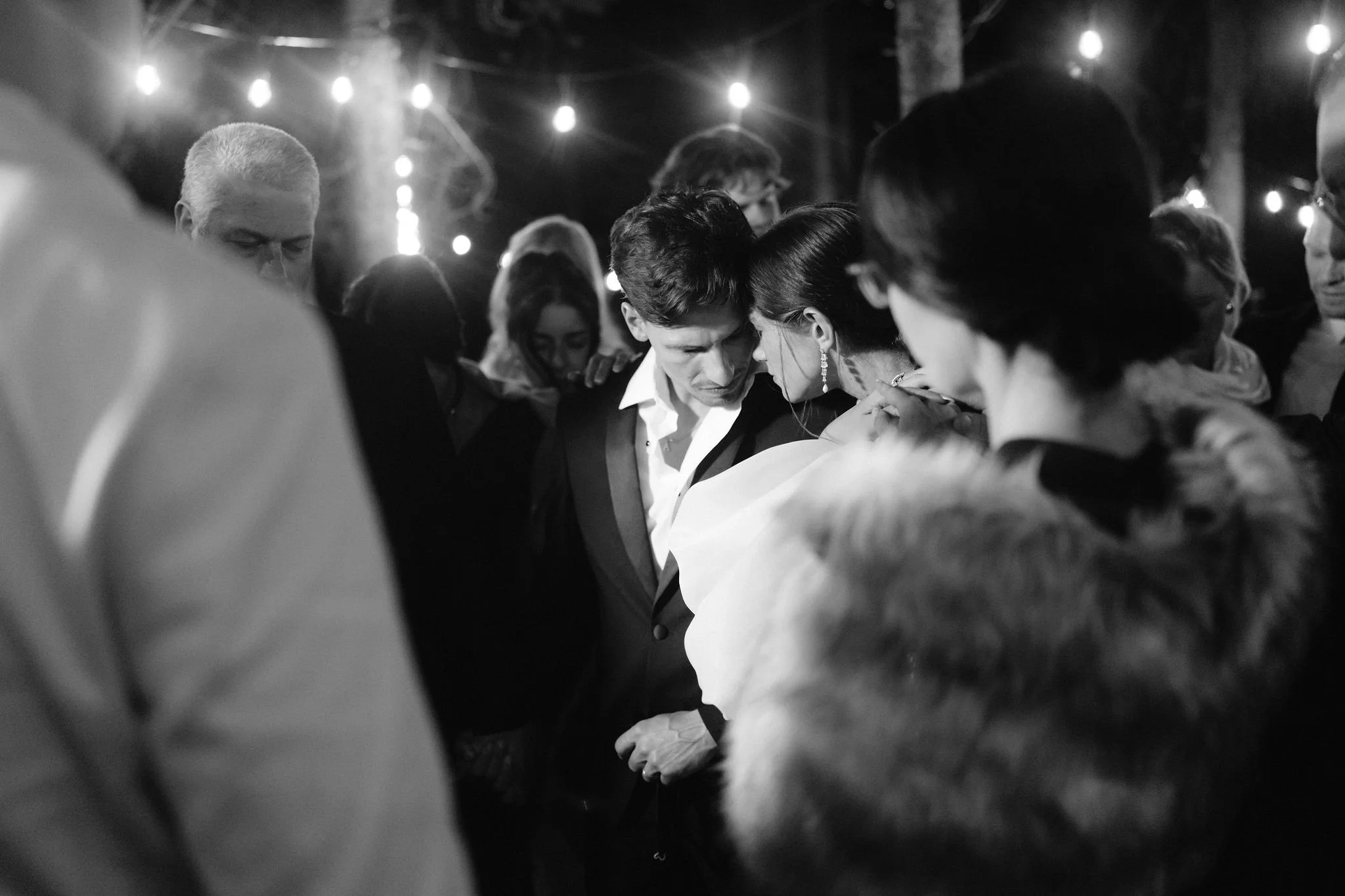 bride and groom in the middle of a circle surrounded by friends and family who have their hands on them and are praying over them