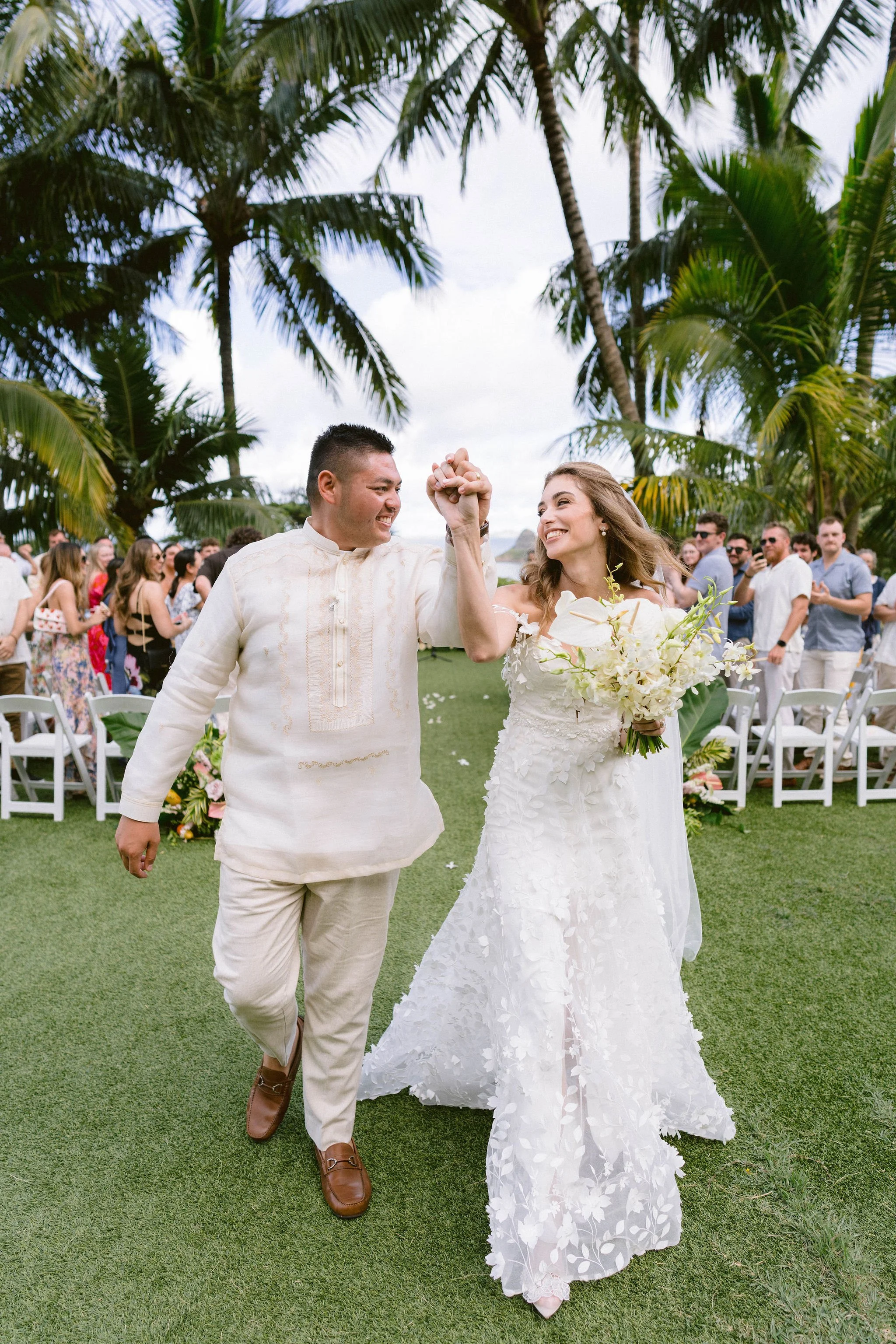 bride and groom joyfully recess down the aisle with hands lifted smiling at each other