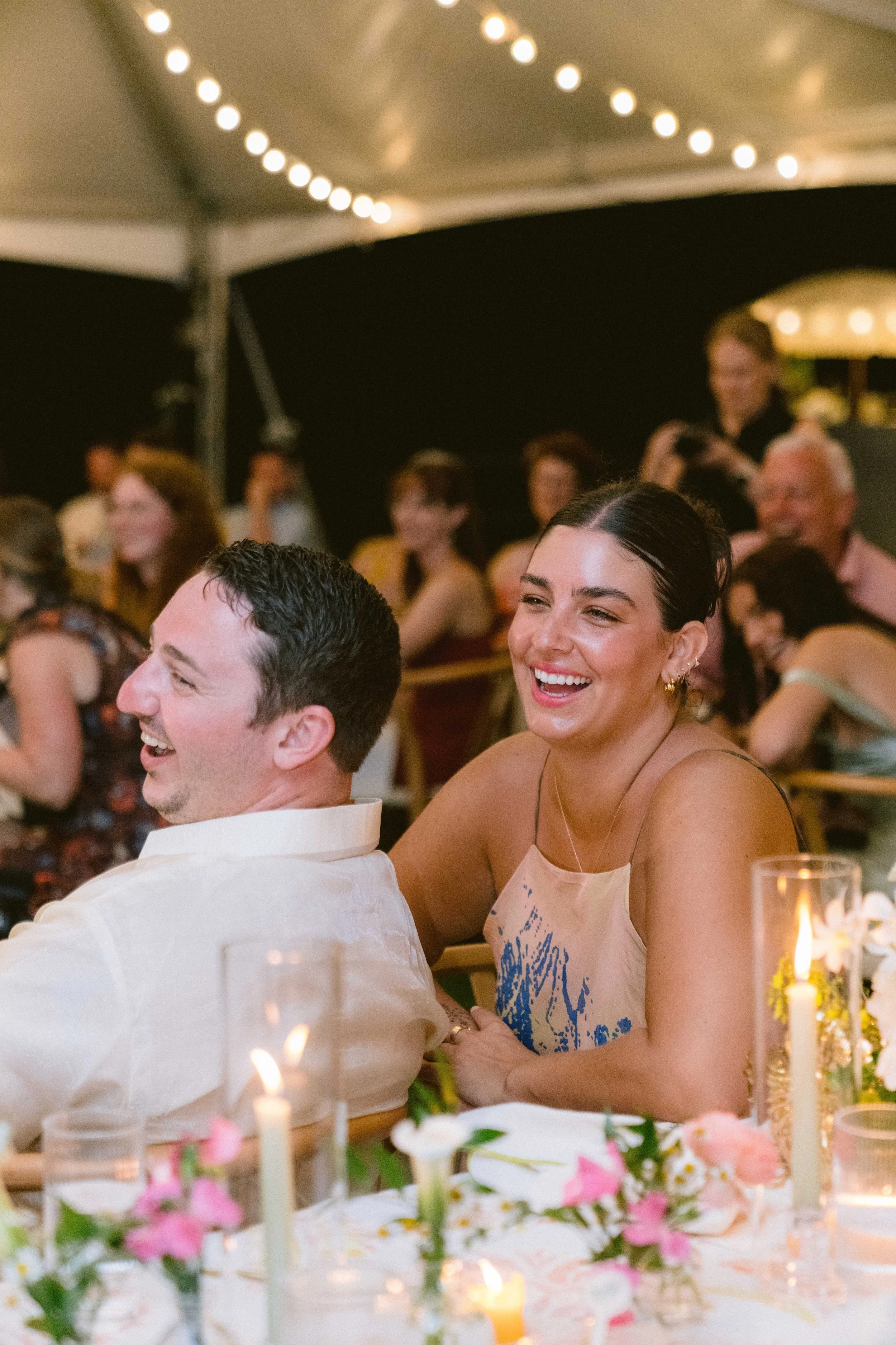 friends laugh while seated for dinner and toasts at wedding