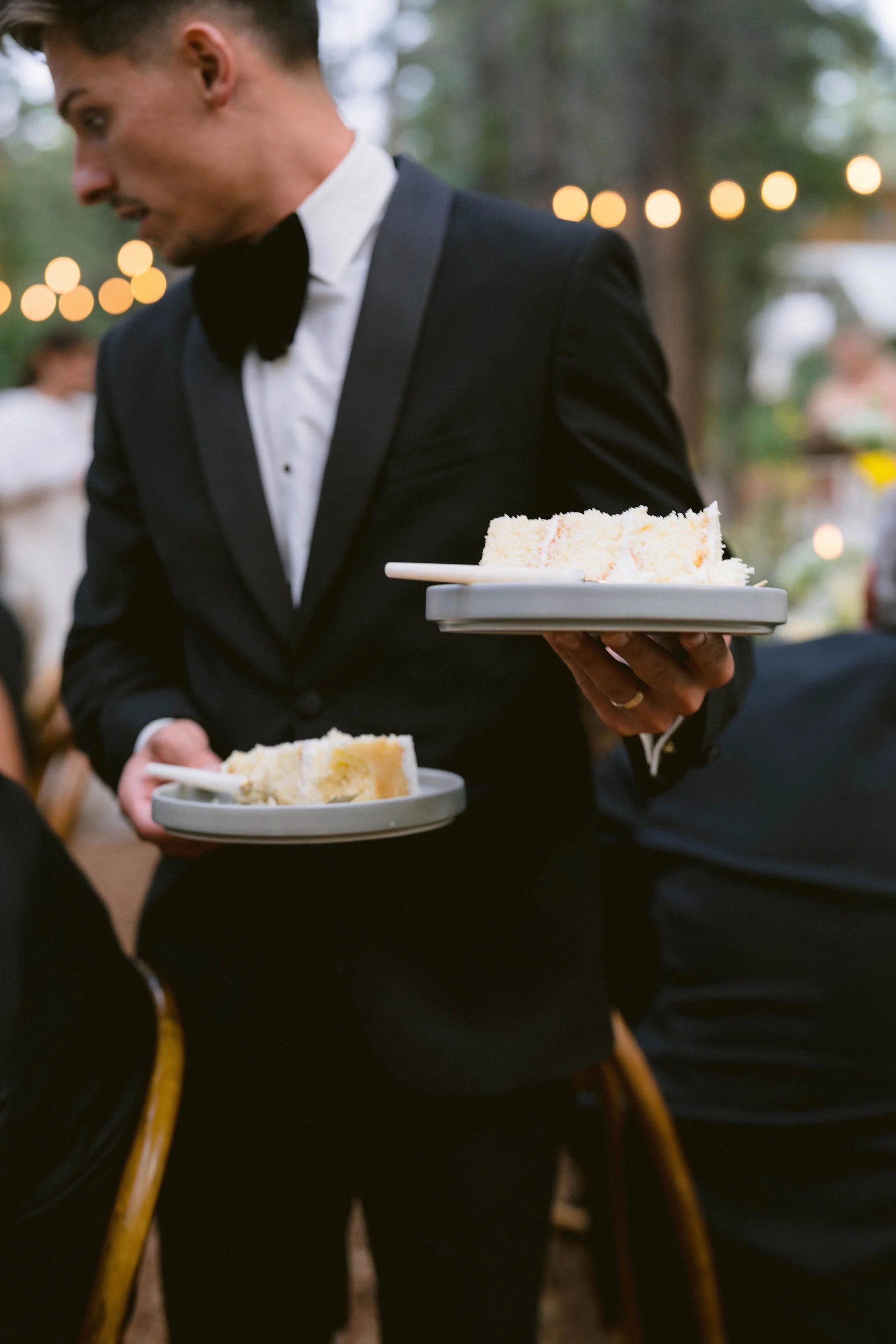 groom holding two plates of wedding cake to serve to guests