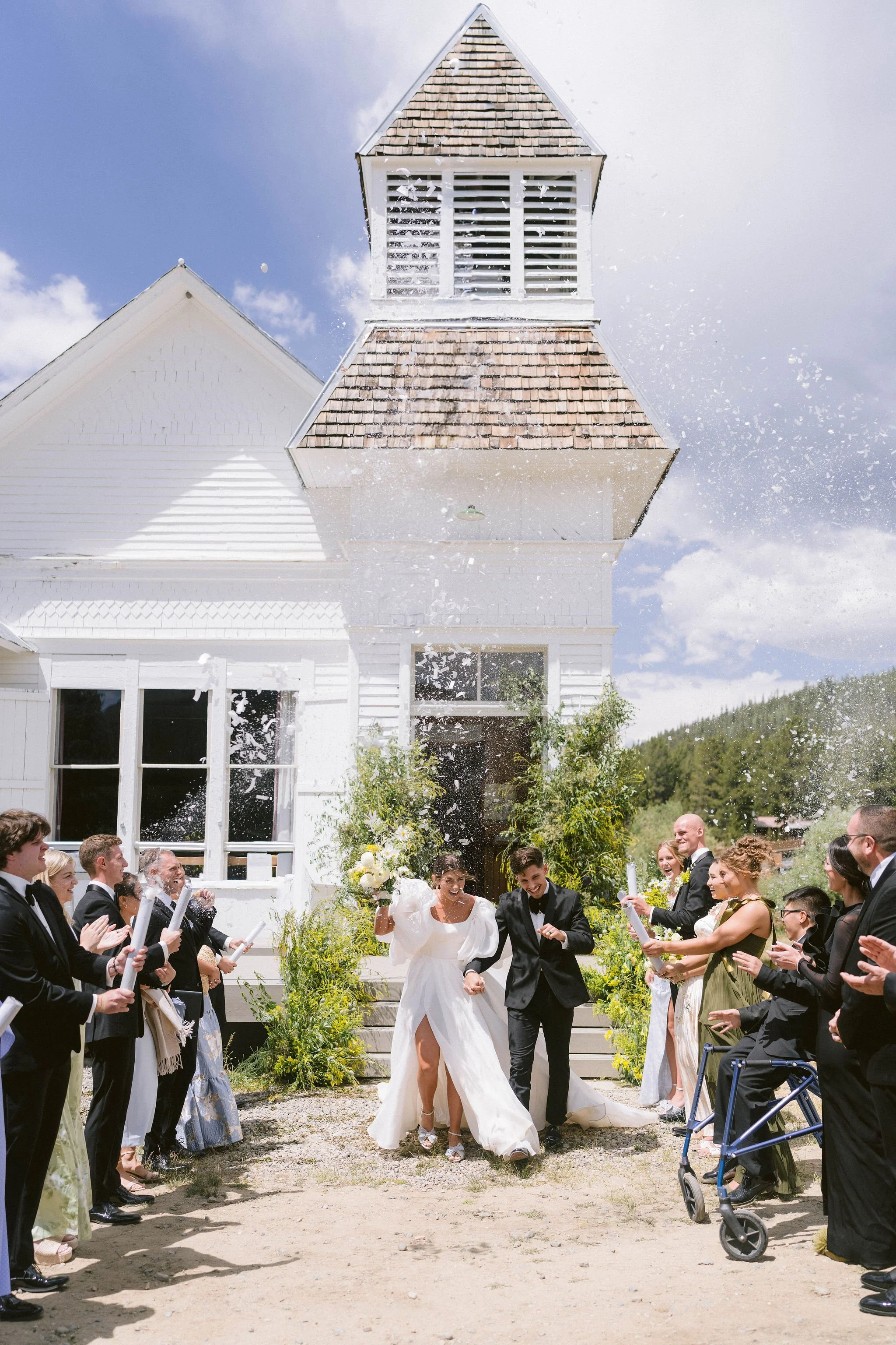bride and groom exit the white chapel in tin cup while friends and family pop confetti cannons and cheer
