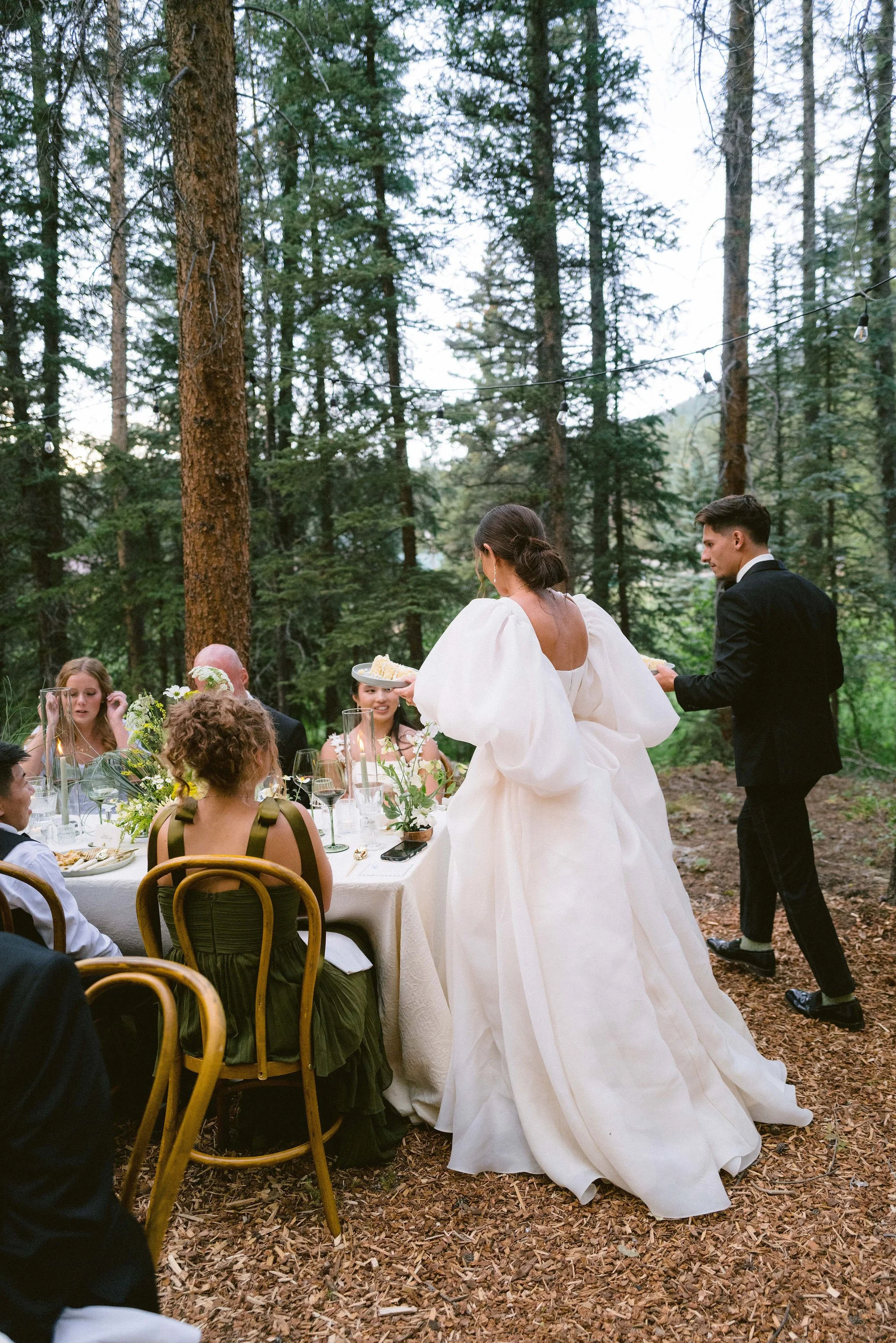 the bride and groom walking up to reception table to serve their guests cake
