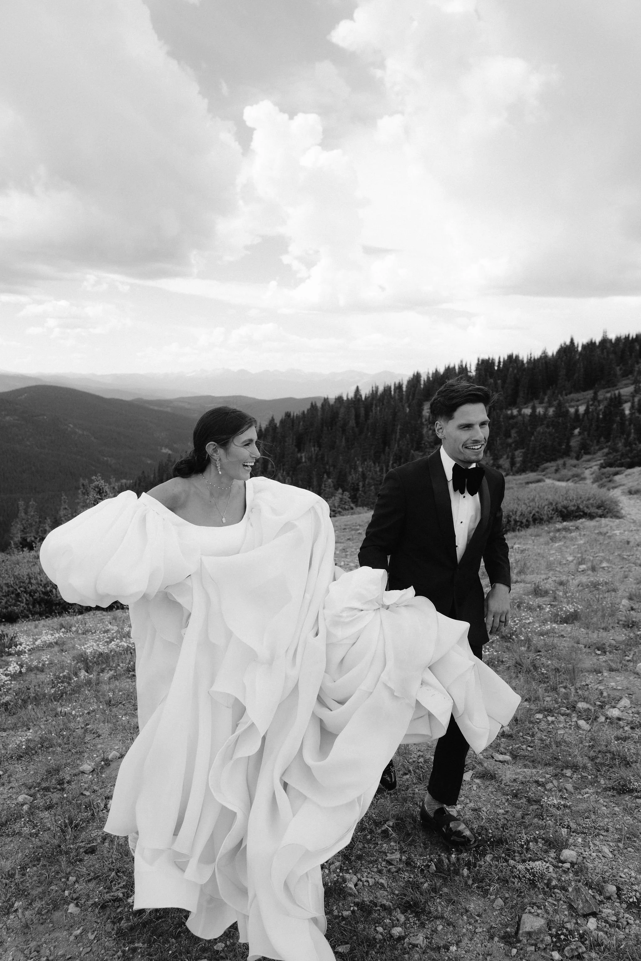 bride and groom laughing at each other as the groom helps the bride carry her dress and walk