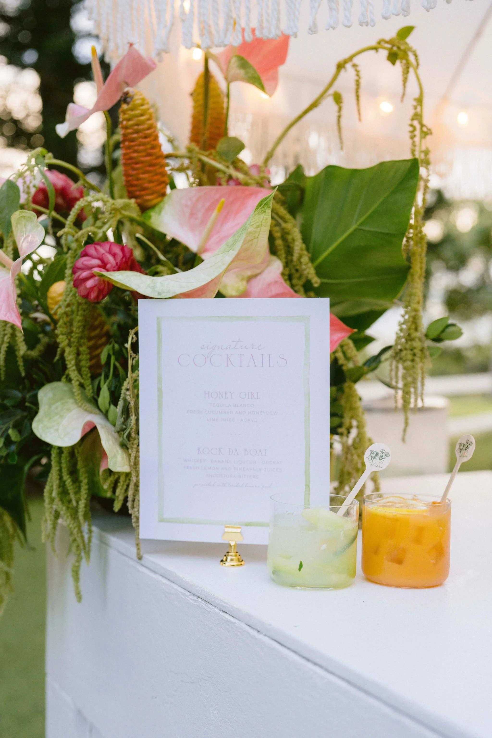 signature drinks and custom bar menu with stunning tropical arrangement behind it