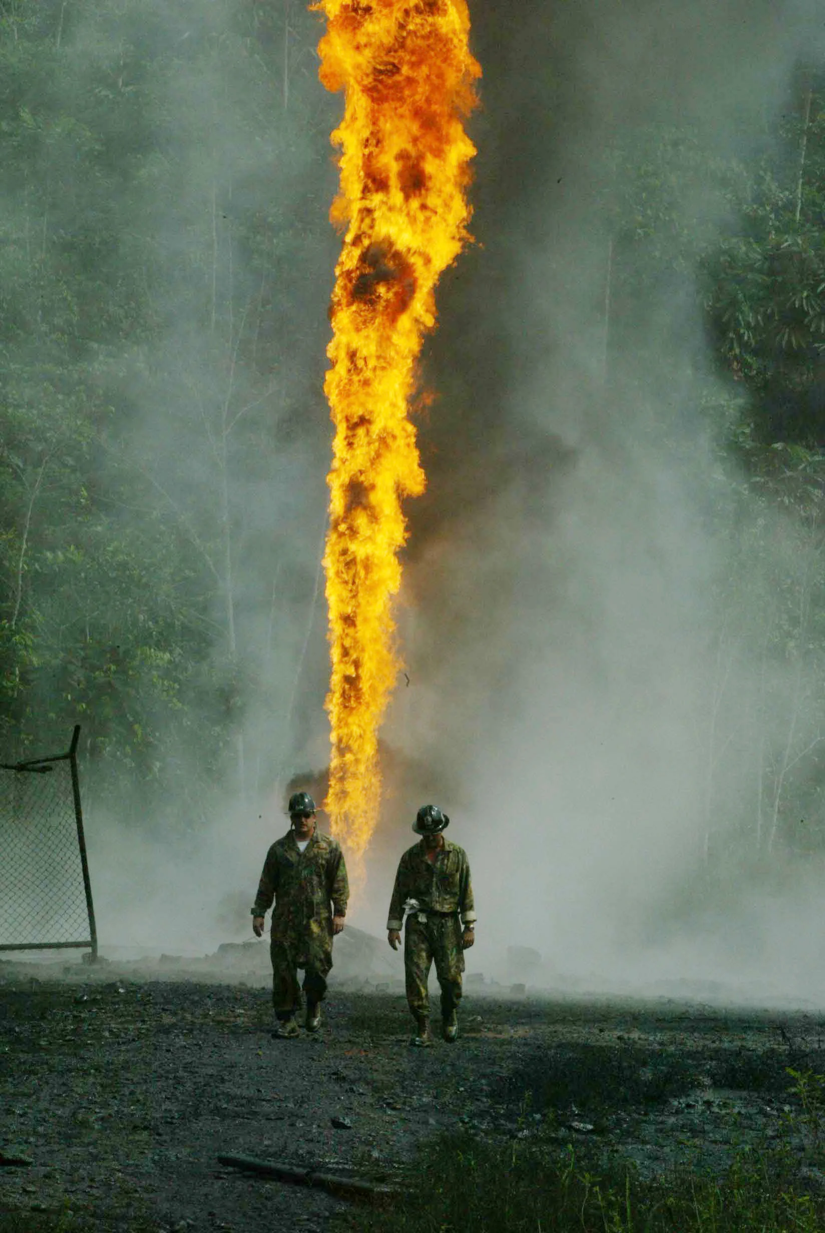 U.S contractors walk next to an oil well set ablaze by rebels in the rural area of Puerto Asis, in the jungles of the southern state of Putumayo, 2003
