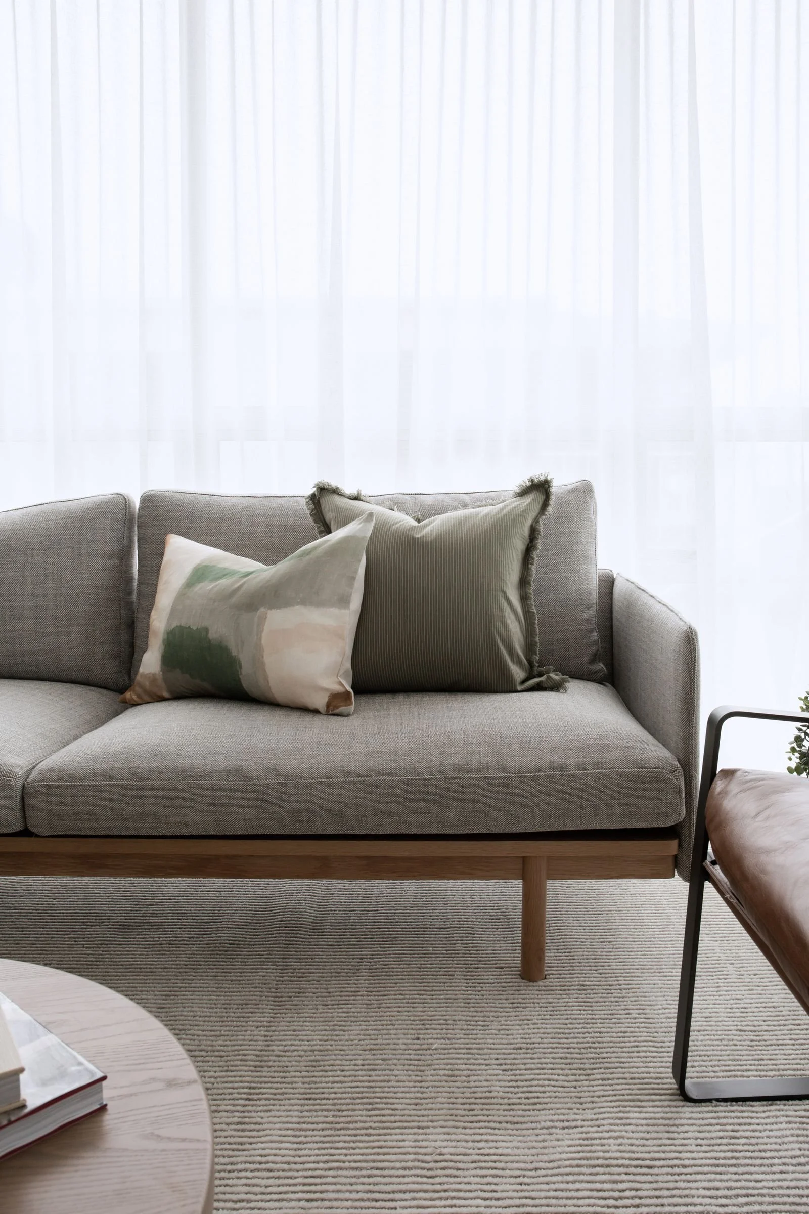 Minimalist grey sofa styled with sage green fringe pillow and abstract print lumbar — curated throw pillow styling