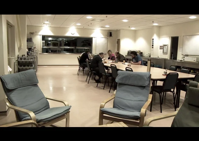 PHOTO CREDIT: The above three images are screenshots from the movie. The top 2 show exterior shots of the base where the workers are staying and working through the winter. The above image is of an interior scene where s ix of the 14 people wintering at the Antarctic research station have their breakfast around a conference table. 