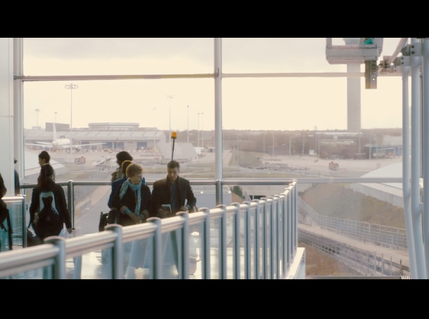 Screenshot from Philomena of Martin and Philomena riding on a luggage cart at Stansted Airport. The large floor-to-ceiling windows at the airport provide a beautiful backdrop and much-needed natural lighting for the film set.