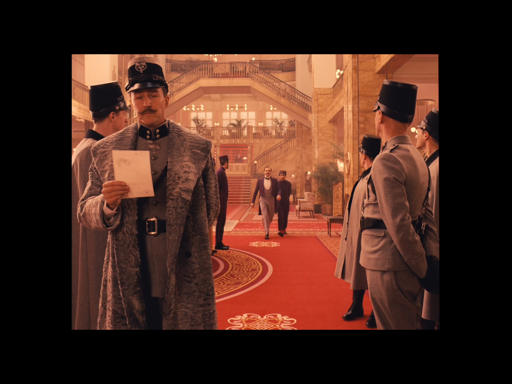A screenshot from the movie of a scene in the lobby of Grand Budapest Hotel during its pinnacle time in the 1930's - with Henckels in the foreground waiting for M. Gustave (who's followed by Zero). The film location of the above scene was also the G…