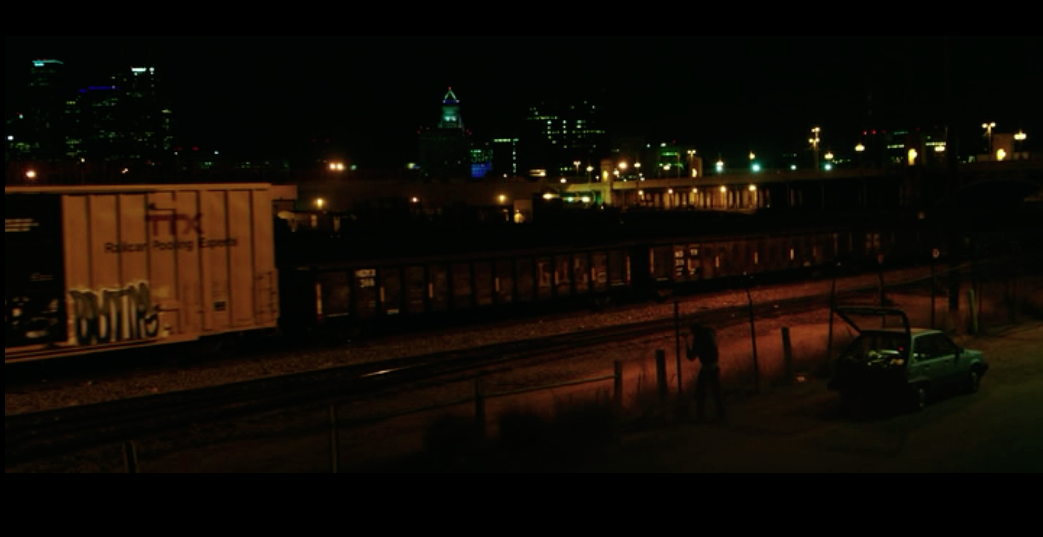 Screenshot from Nightcrawler of a scene at the beginning at the movie at the train track with the Los Angeles skyline twinkling in the background.
