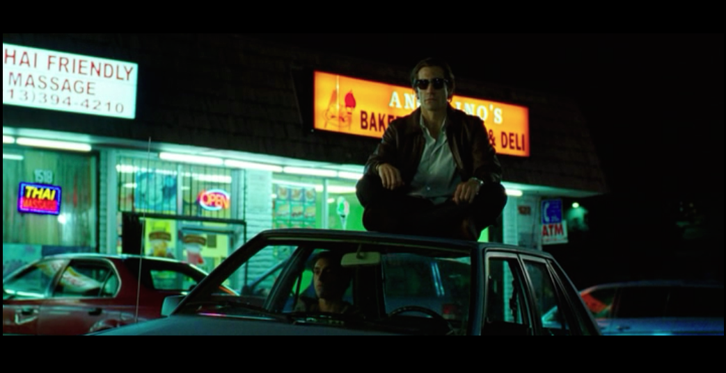 Screenshot from Nightcrawler of a scene filmed in front of Angelino's Bakery on West Sunset Blvd - featuring Lou Bloom sitting on top of his car and Rick (his employee/intern) sitting inside the car - both waiting for a crime to happen so they can be first to cover it.
