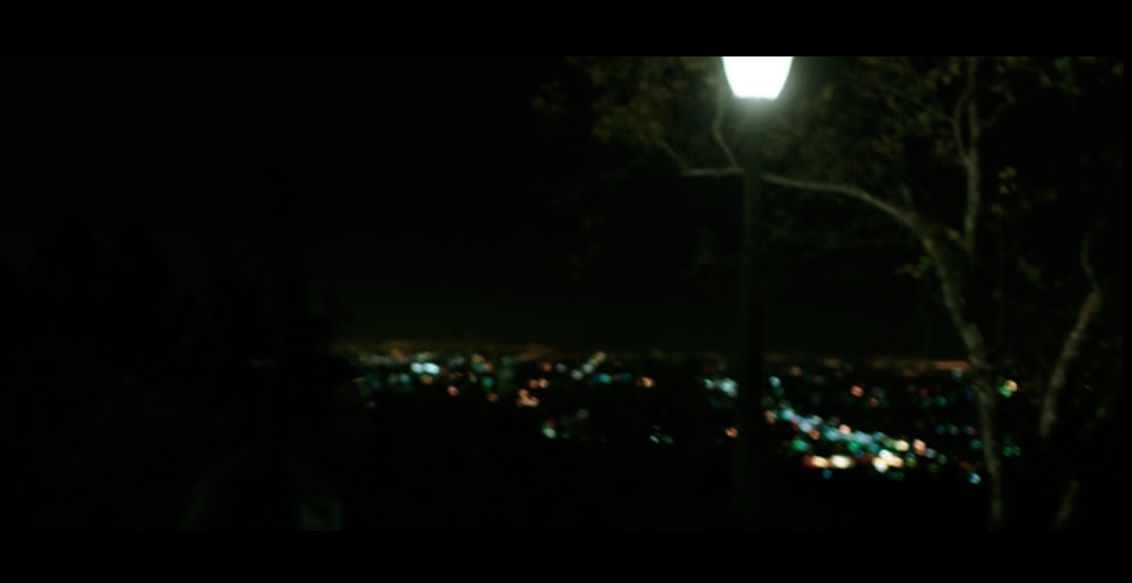 Screenshot from Nightcrawler of a scene filmed on Mulholland Drive with the twinkling lights of Los Angeles in the valley below.