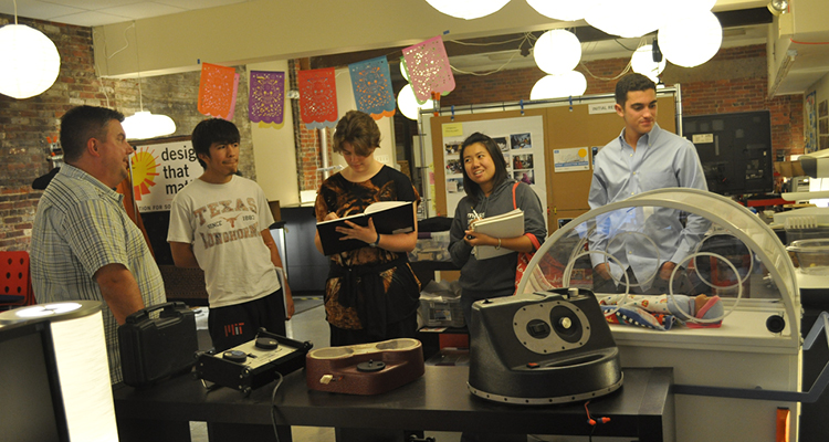 MIT students Isaac Sosa, Kristen Zimmerman, Joanna So, and Eduardo Bacardi visit DtM to see the MIT 2.009 team’s Kinkajou Projector (forefront), and to learn about the successes and failures of DtM’s NeoNurture Infant Incubator (right).