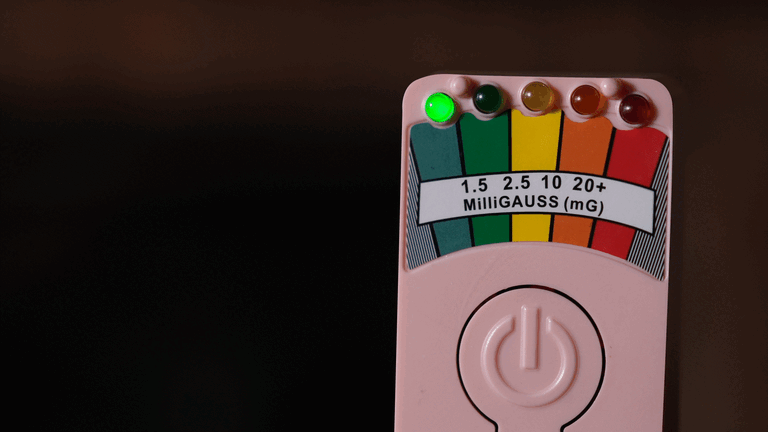 A pink radiation detector showing a green light on the low radiation level side, with the needle slightly pointing to the green zone.