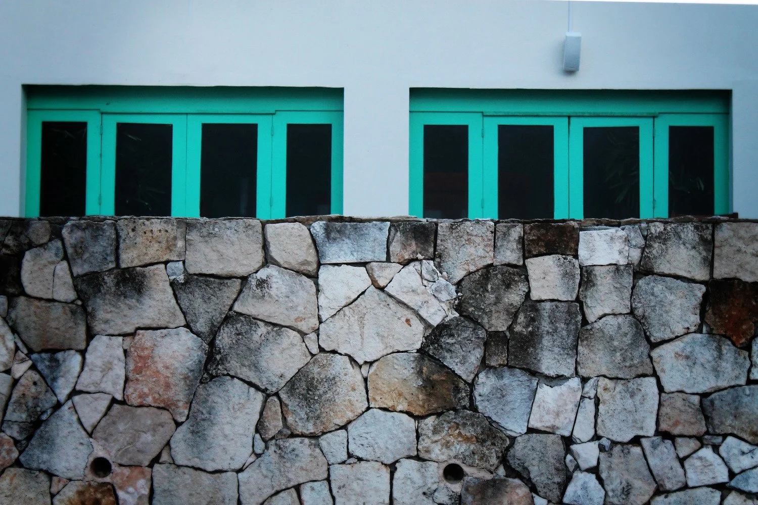 Green-framed windows behind a stone wall on a white building exterior.