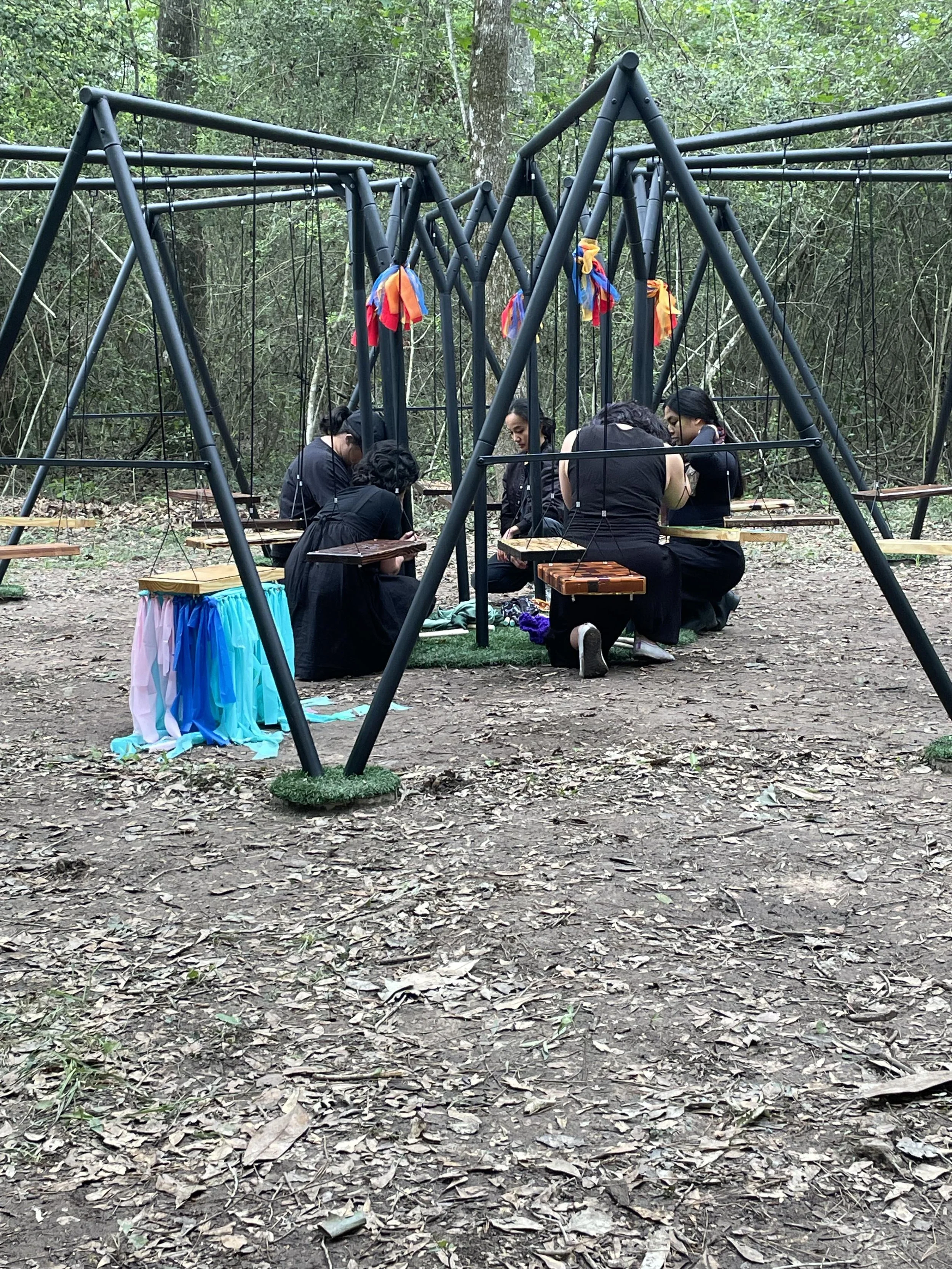Group of people kneel or squat in the center of a large, metal playset.