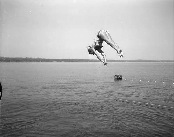 Caption on a photo dated July, 1955, reads, "Tia Nelson, 11, daughter of Mr. and Mrs. Russell Nelson...dives into Lake Mendota. She was one of Madison's most outstanding young swimmers."