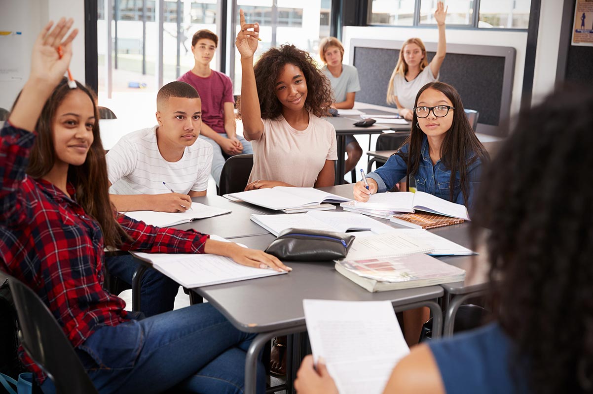 High school students raise their hands to ask their teacher questions about the Common App essay