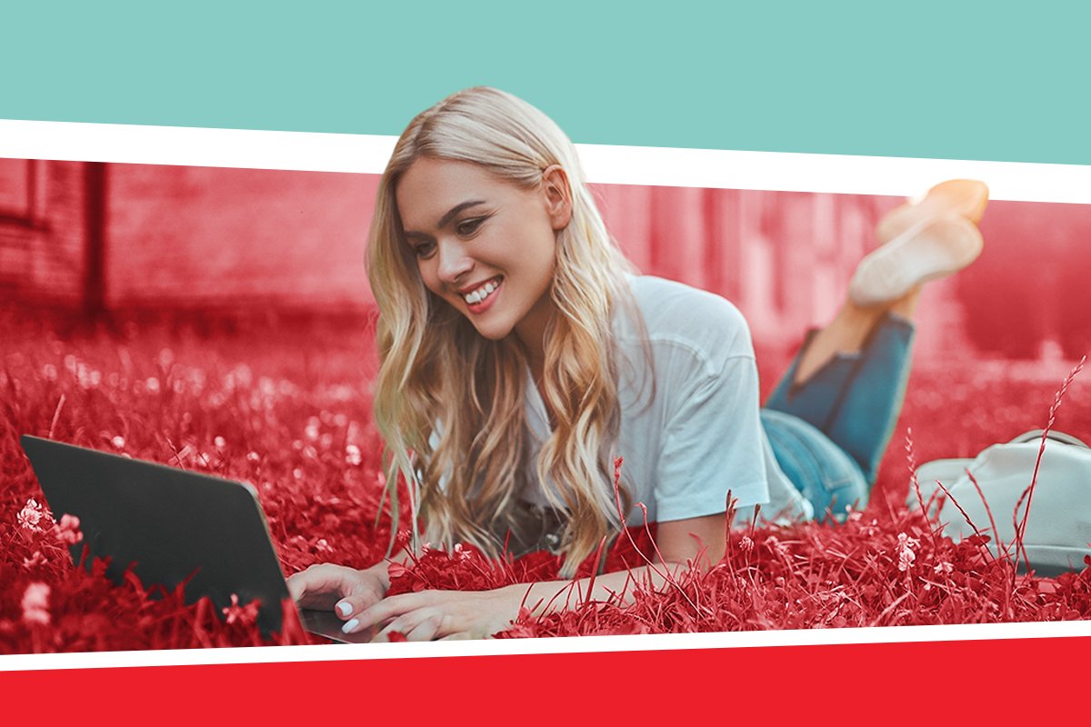 A smiling USC student using a laptop and laying in the grass