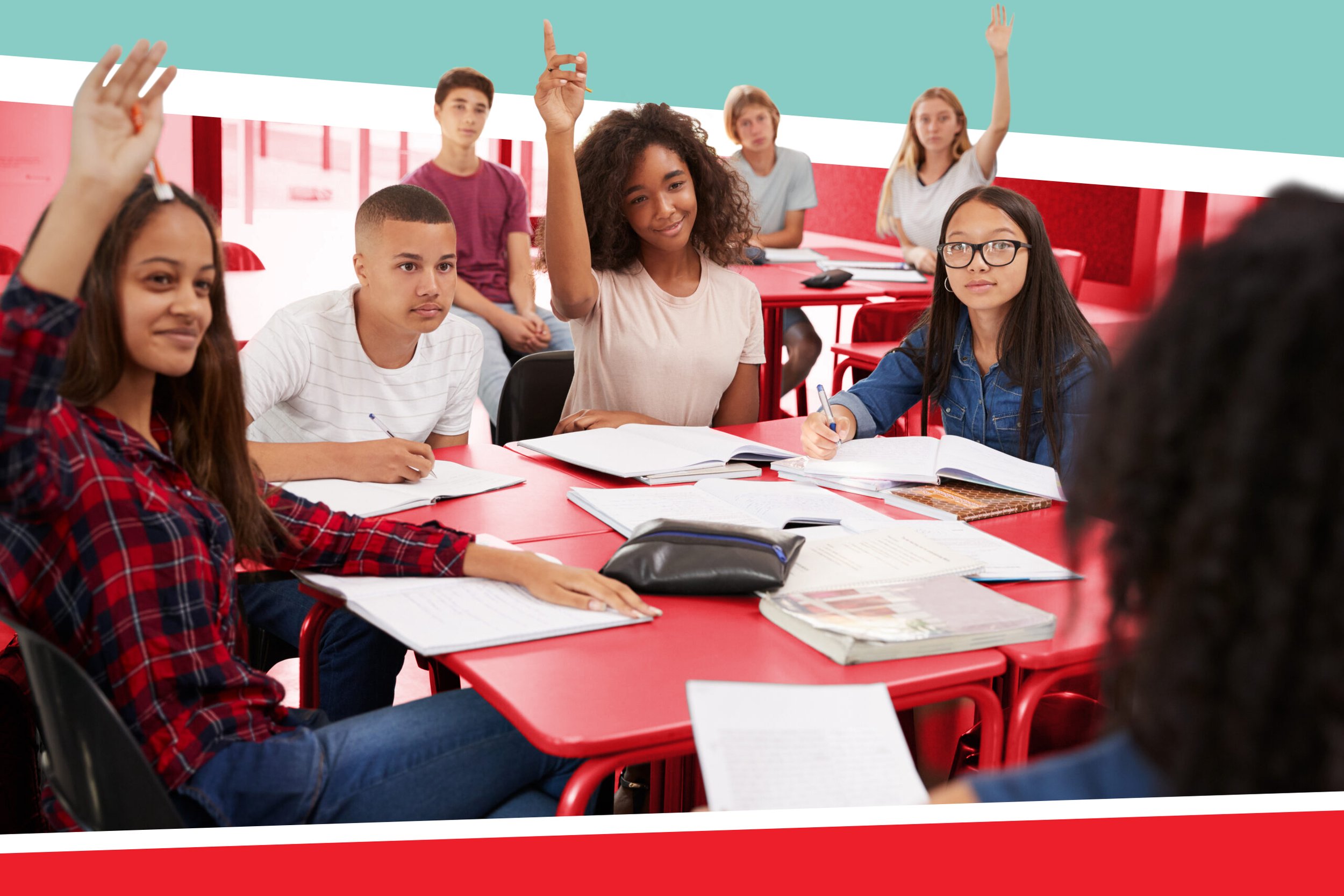 A group of students sitting at tables with notebooks raising their hands