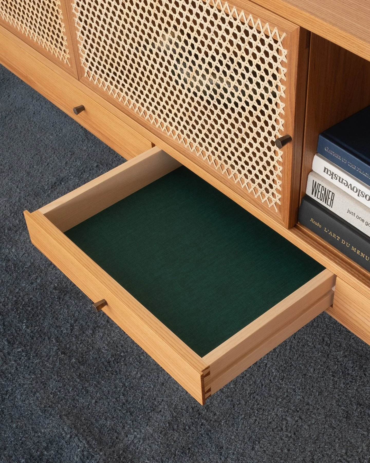 All the details. The Plait cabinet (formerly Tinselor) in elm with cane doors, brass knobs, and book cloth clad drawer bottoms.