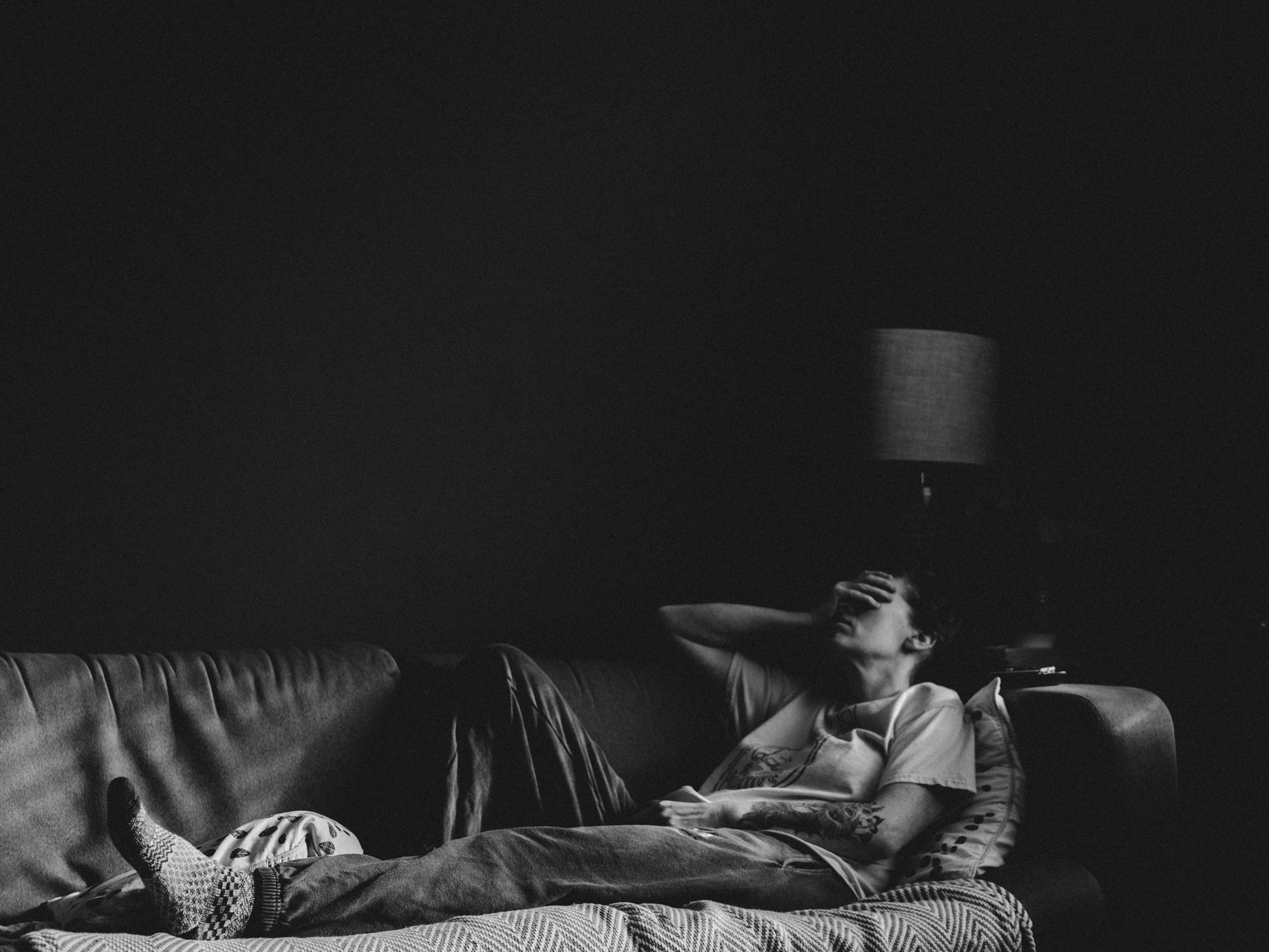 black and white photo of a man sitting across a couch with his hand over his eyes