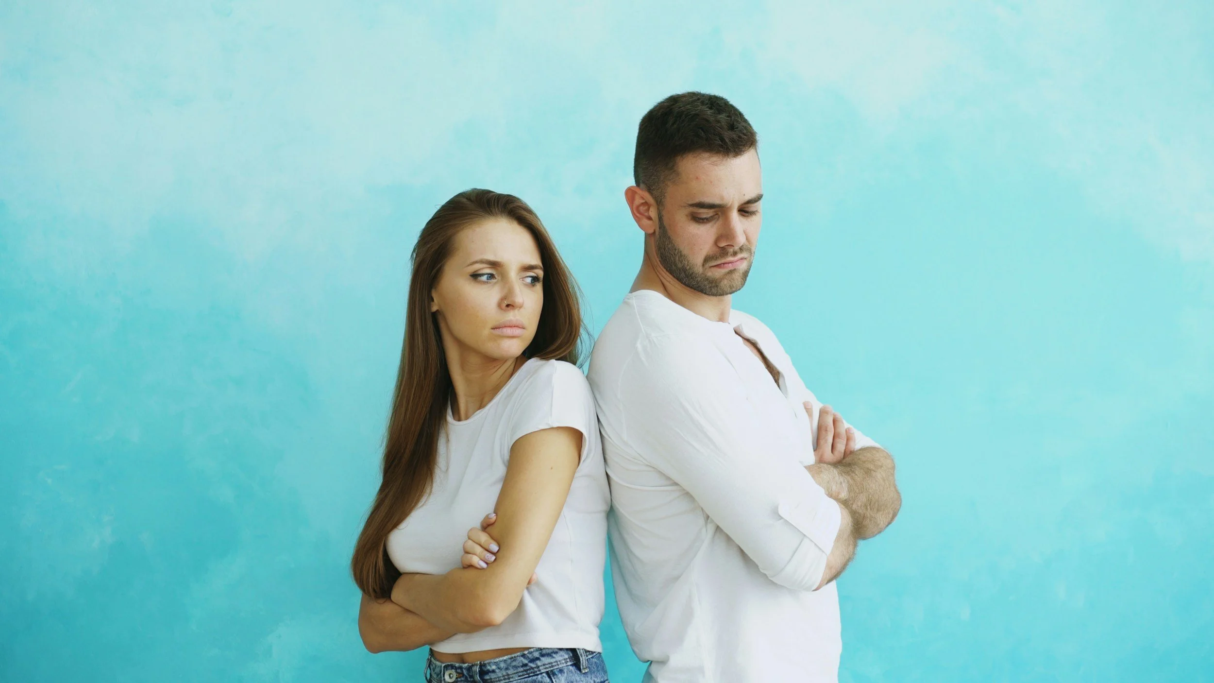woman and man in white shirts standing back to back with looks of irritation with one another