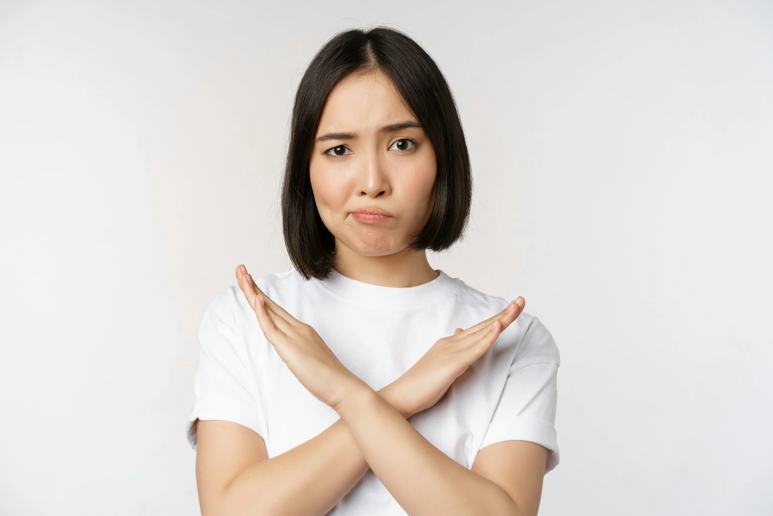 woman with a brown bob haircut in a white t-shirt with her hands across her chest in the shape of an X