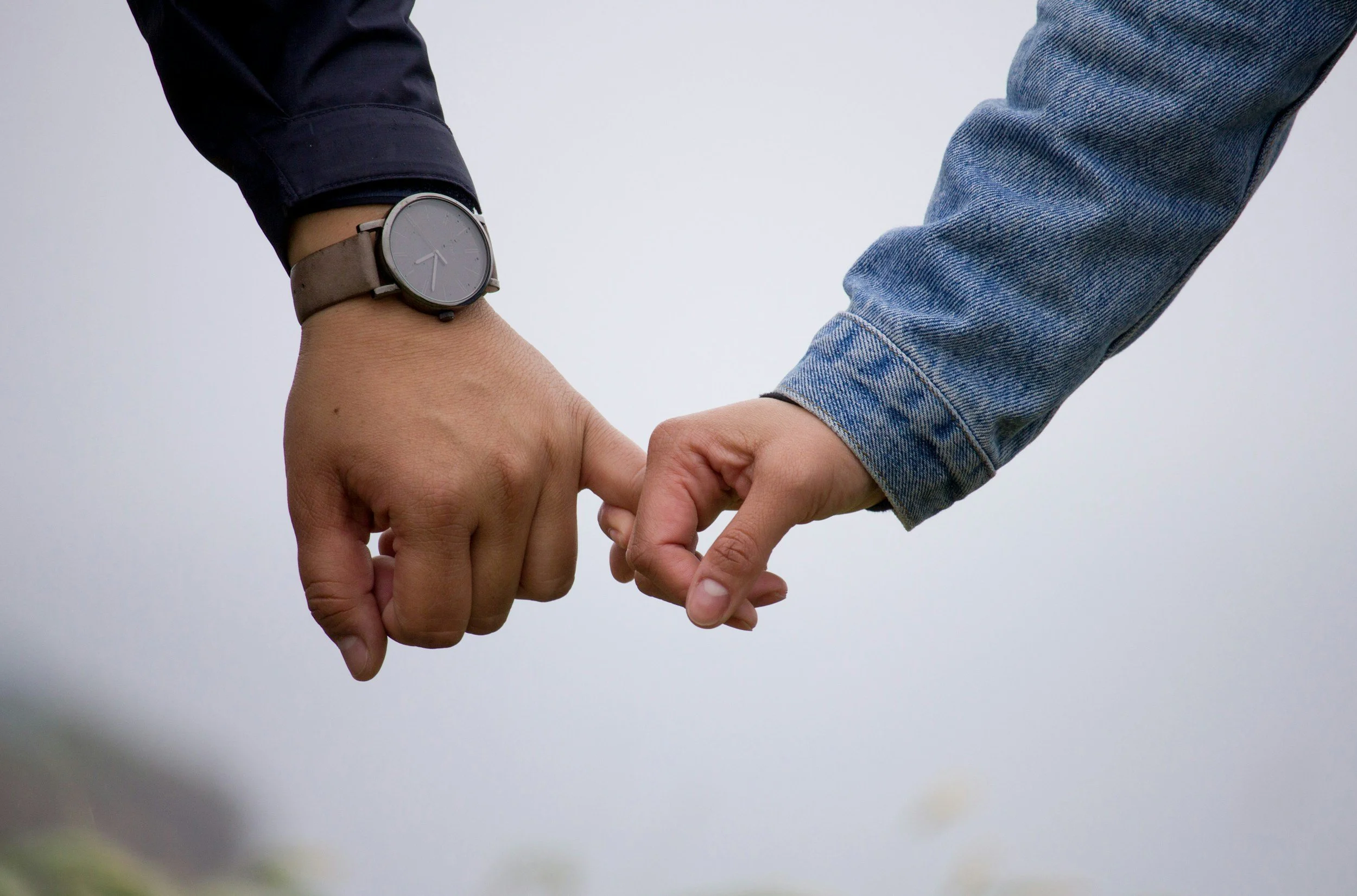 a hand with a watch and black sleeve holding pinkeye tie a smaller hand with a jean sleeve