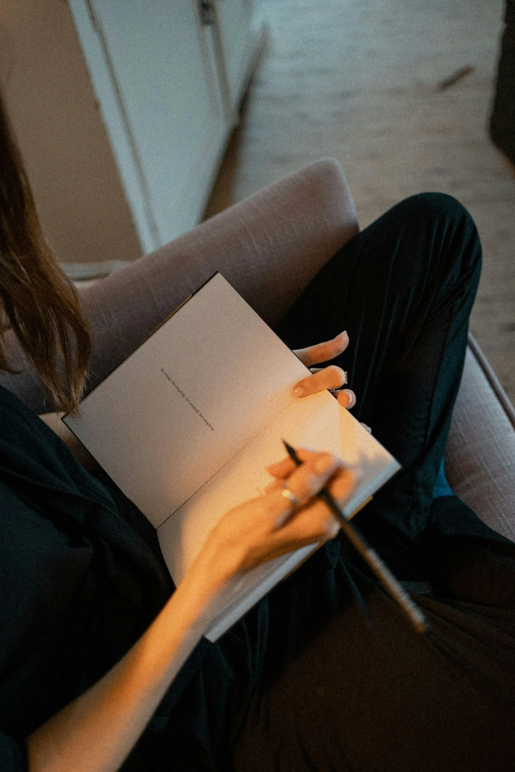woman's hands holding a journal and pen in her lap with her legs crossed