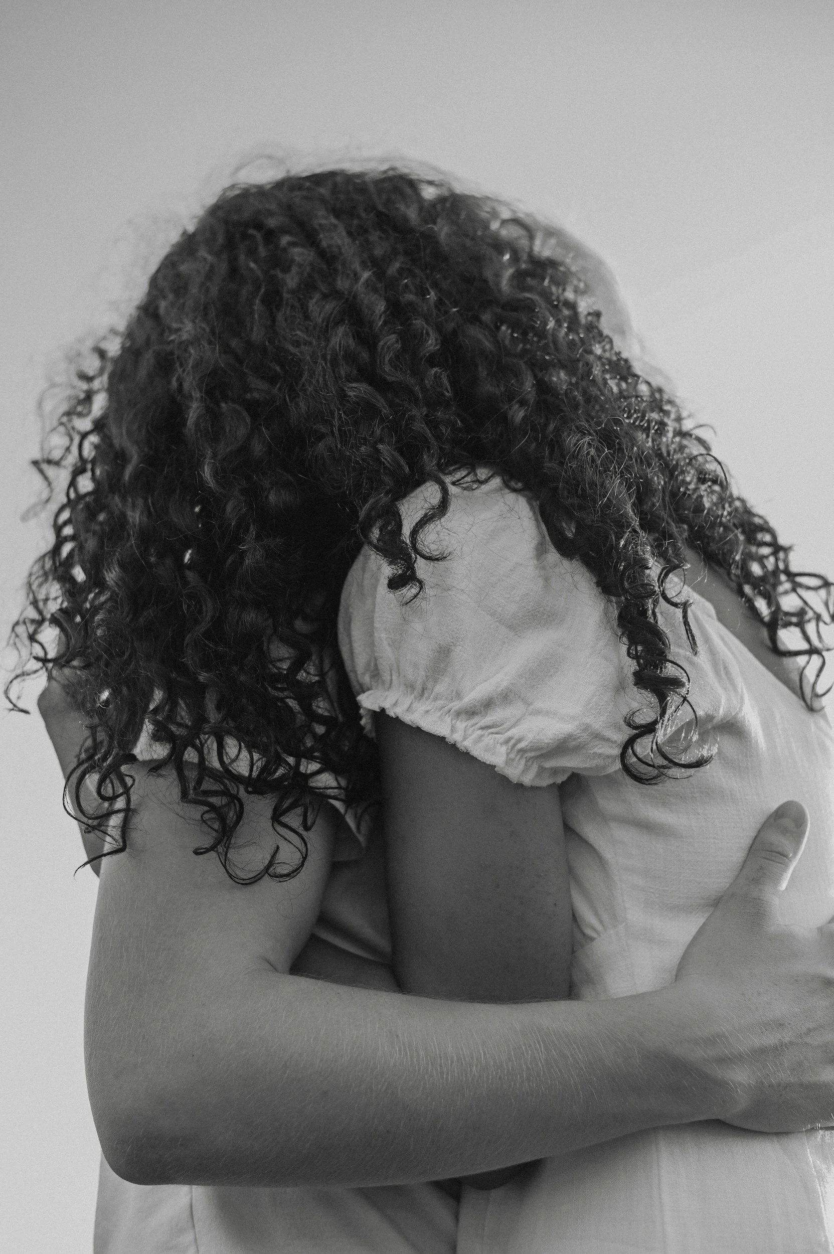 black and white photo of a woman with dark curls being held by another women representing the power of community healing