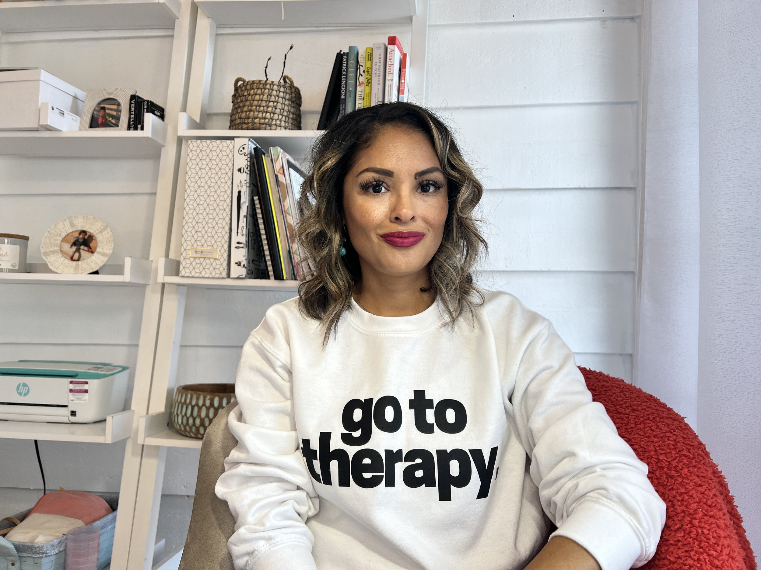 Alicia Taverner is a bipoc therapist wearing a sweatshirt that says "go to therapy"  Alicia is a couples therapist in Calfornia