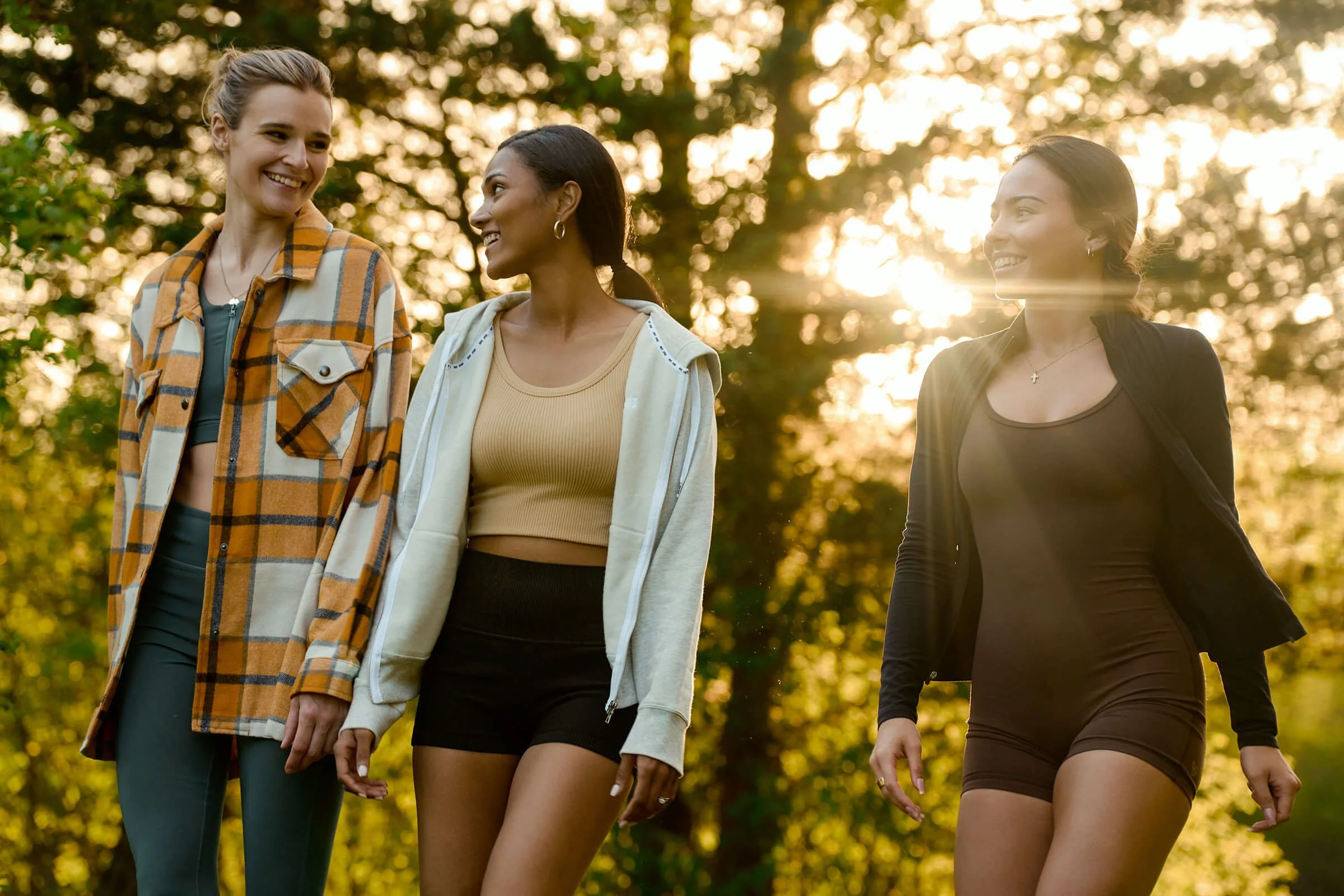 Three women walking outdoors in a park at sunset, smiling and chatting.